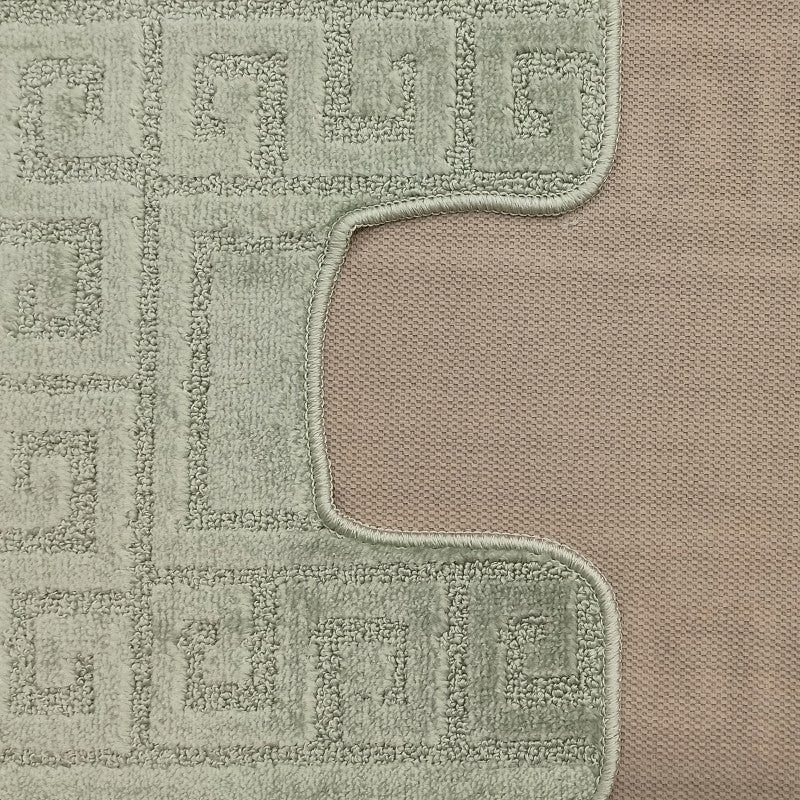 Gros plan sur un tapis vert d'eau avec un motif de méandres grecs en relief. Une découpe montre son envers beige tissé