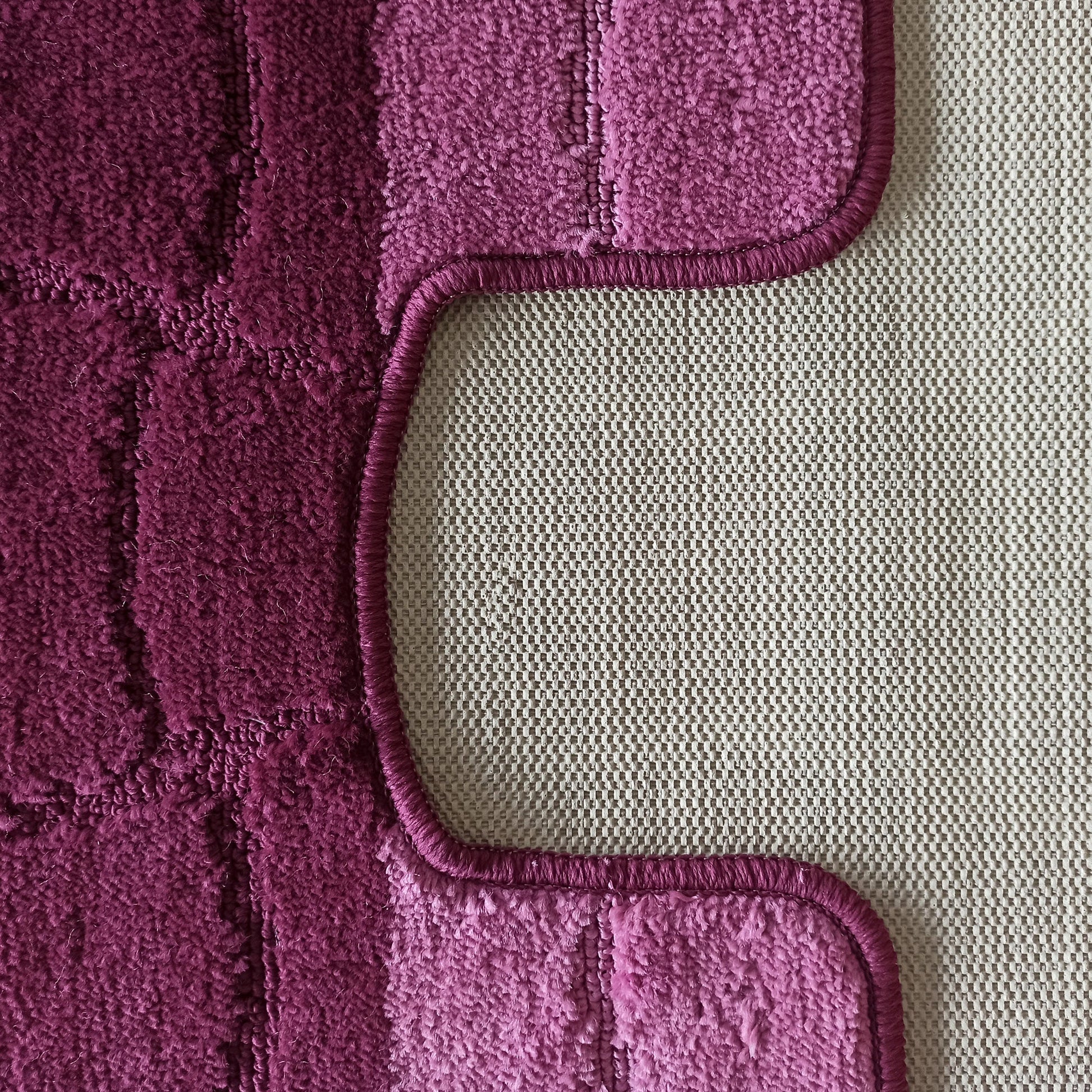 Tapis aux teintes magenta et pourpre à texture bouclée et motifs en relief, avec un bord arrondi sur un fond beige à motif quadrillé