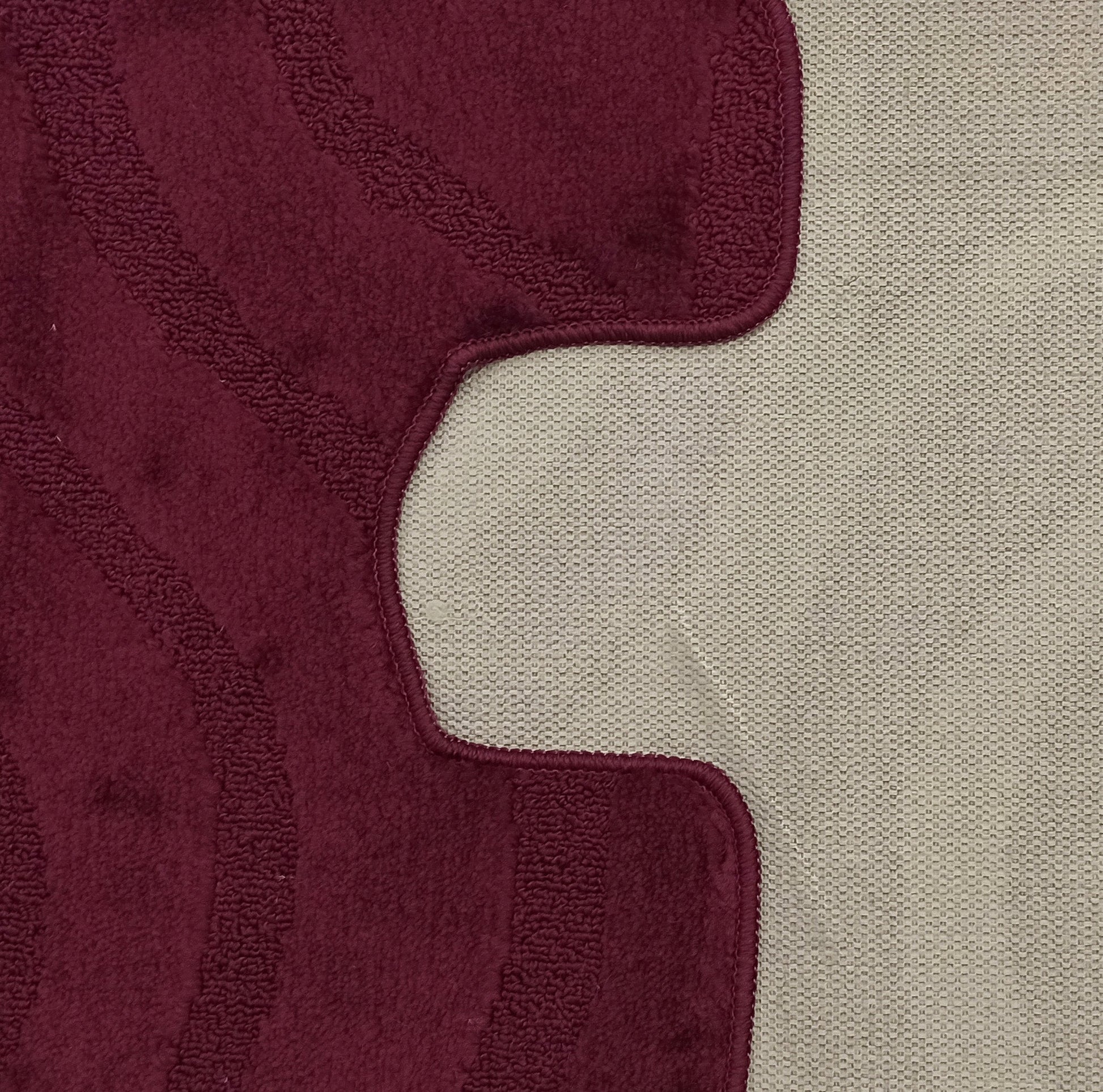 Tapis bordeaux à texture douce et motifs ondulés en relief, avec un contour irrégulier sur fond beige tissé