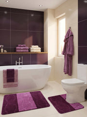 Deux tapis de bain moelleux, un rectangulaire et un en U, violet foncé et mauve clair avec motifs texturés, dans une salle de bain