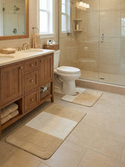 Tapis de bain rectangulaire beige et crème, avec des bandes de couleur et un motif quadrillé texturé, dans une salle de bain