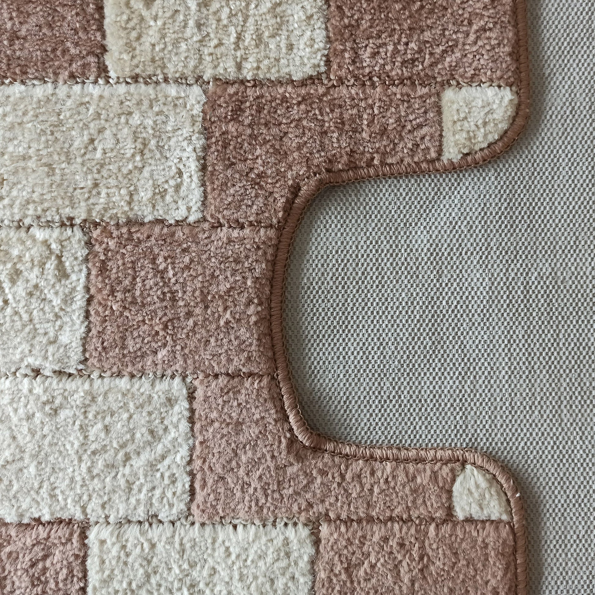 Tapis à longs poils avec motif damier beige crème et rose poudré. Son bord incurvé révèle un fond gris texturé