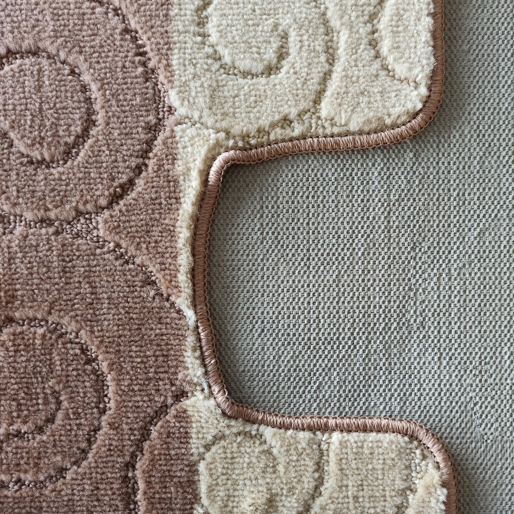 Tapis doux et moelleux aux motifs circulaires et ondulés beige et rose, avec une bordure cousue, posé sur une surface quadrillée grise