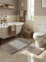 Lot de tapis de bain moelleux taupe et beige clair avec motifs tourbillonnants, posés sur un sol carrelé dans une salle de bain lumineuse