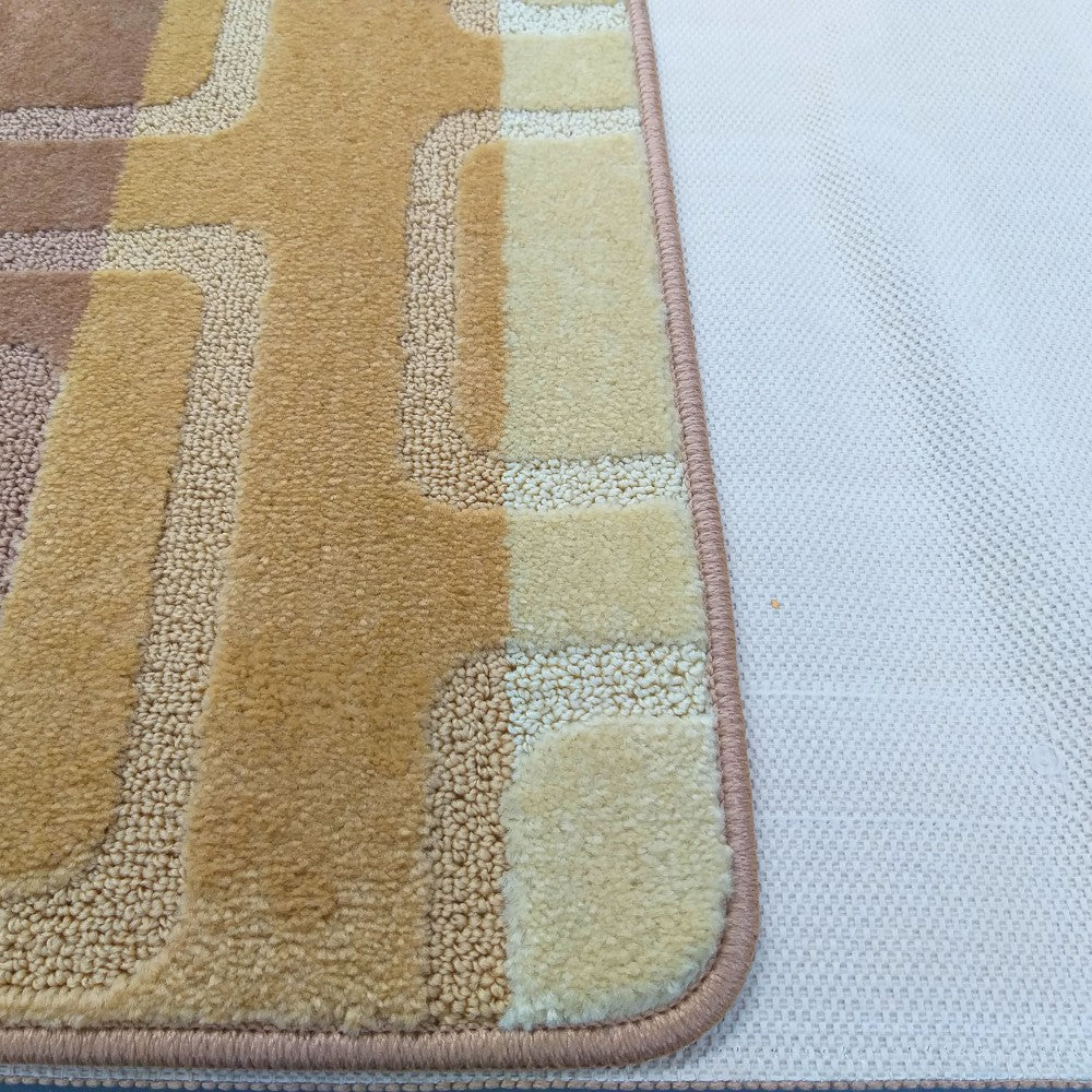 Tapis à motifs géométriques en relief, aux tons de beige, crème et marron clair, avec une bordure rose et son dos antidérapant