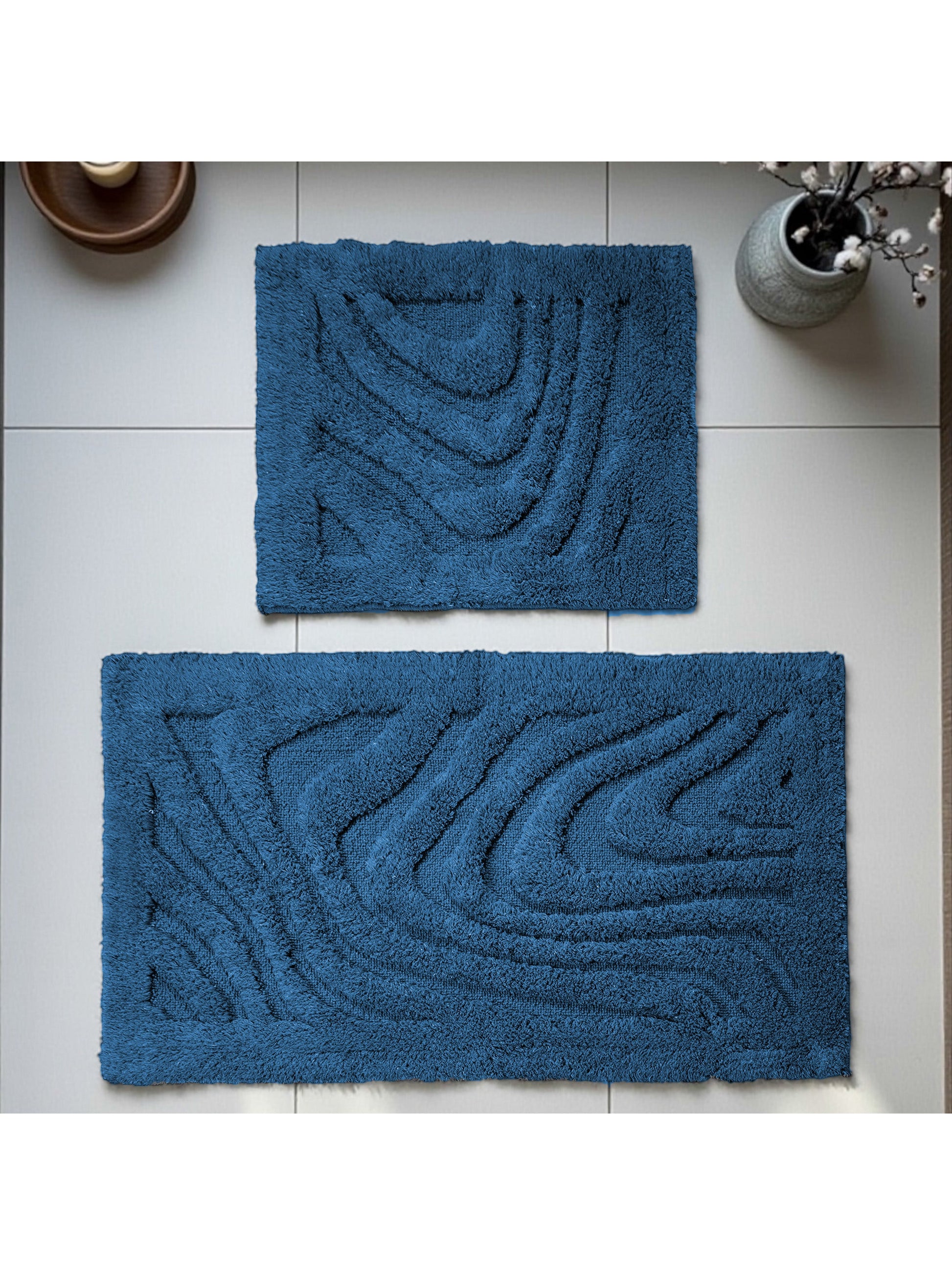 Deux tapis bleus foncés à la texture moelleuse avec des motifs abstraits en relief, sur un sol carrelé clair