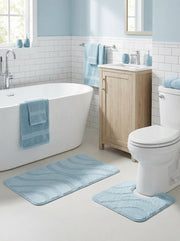 Deux tapis de bain bleus avec des motifs ondulés, l'un rectangulaire et l'autre en U, posés dans une salle de bain lumineuse