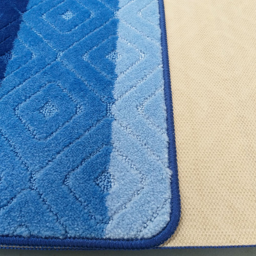 Tapis doux aux motifs de losanges bleus dégradés, du foncé au clair, bordé de bleu foncé, avec une sous-couche beige visible