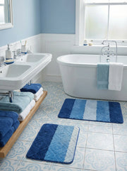 Deux tapis de bain rectangulaires à rayures dégradées du bleu foncé au bleu clair et blanc, ornés de motifs losanges texturés, sont posés sur le sol carrelé d'une salle de bain