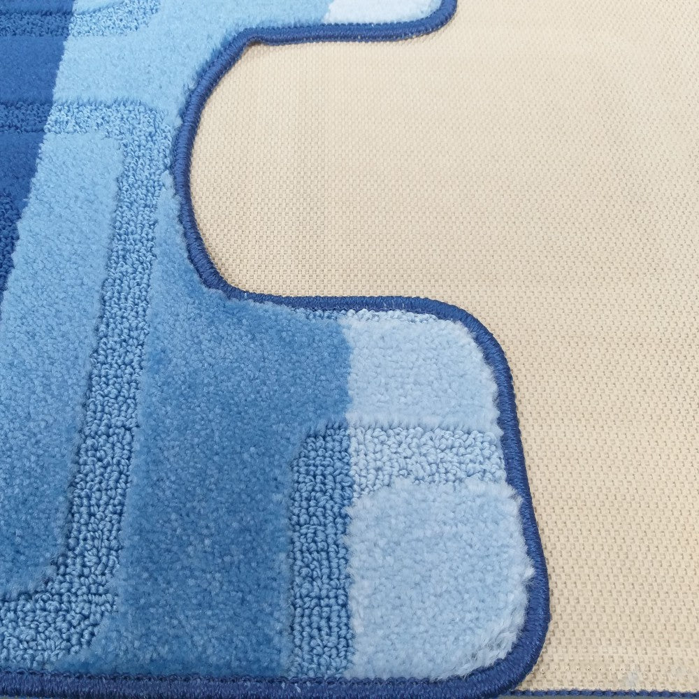 Tapis texturé bleu avec des zones de couleurs claires et foncées, un contour irrégulier brodé sur un fond beige