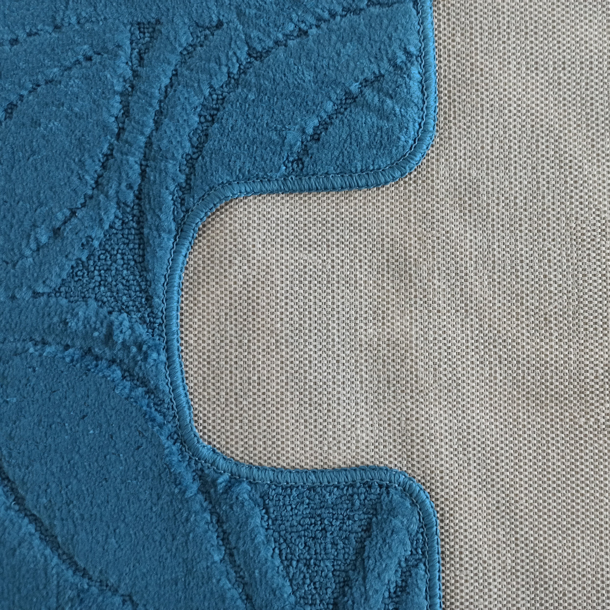 Gros plan d'un tapis bleu turquoise texturé avec motif de feuilles en relief, délimité par une couture sur une surface beige tissée