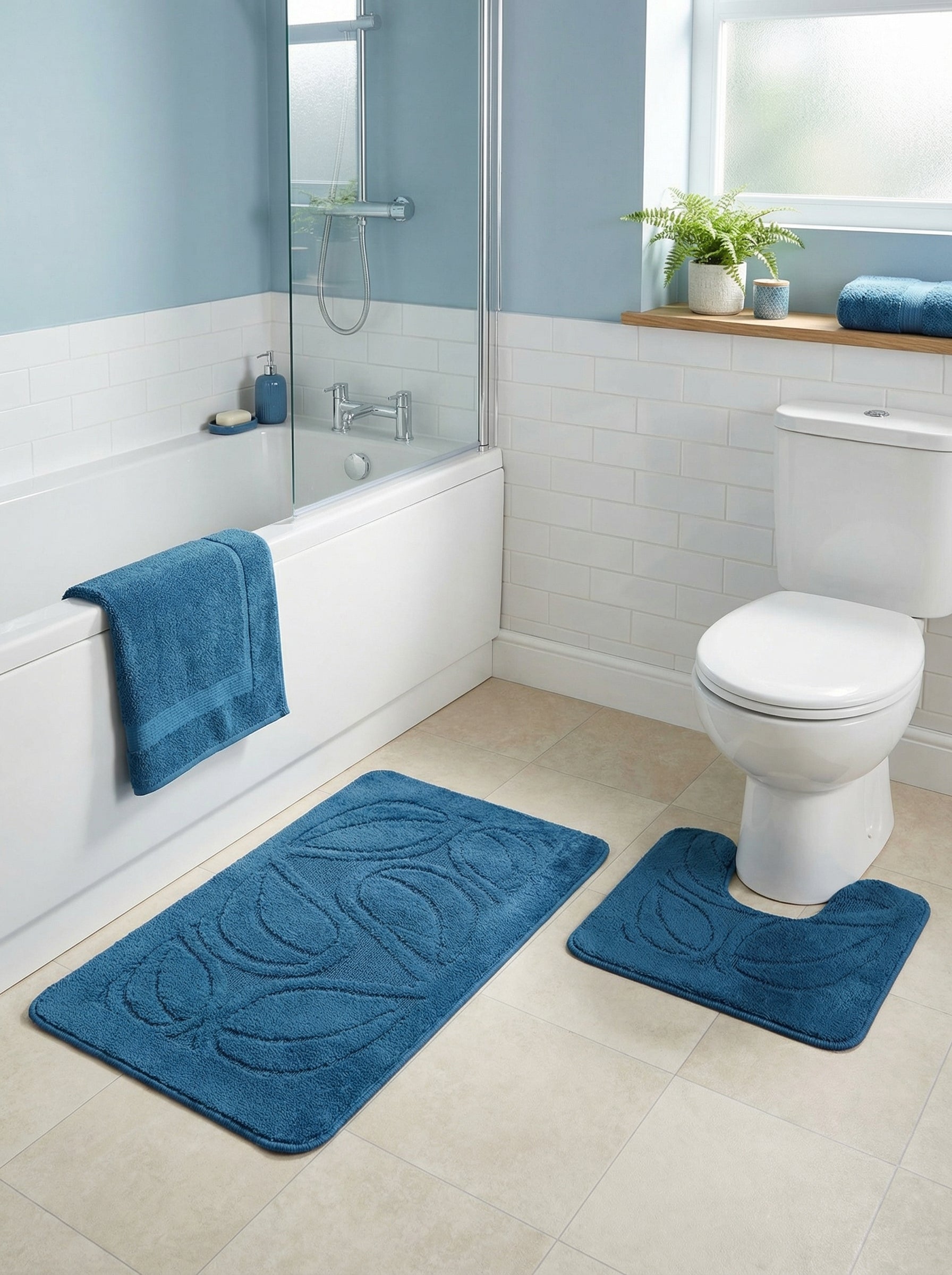 Deux tapis de bain bleu sarcelle moelleux à motifs de feuilles, un rectangulaire et un en U, sur le sol carrelé d'une salle de bain