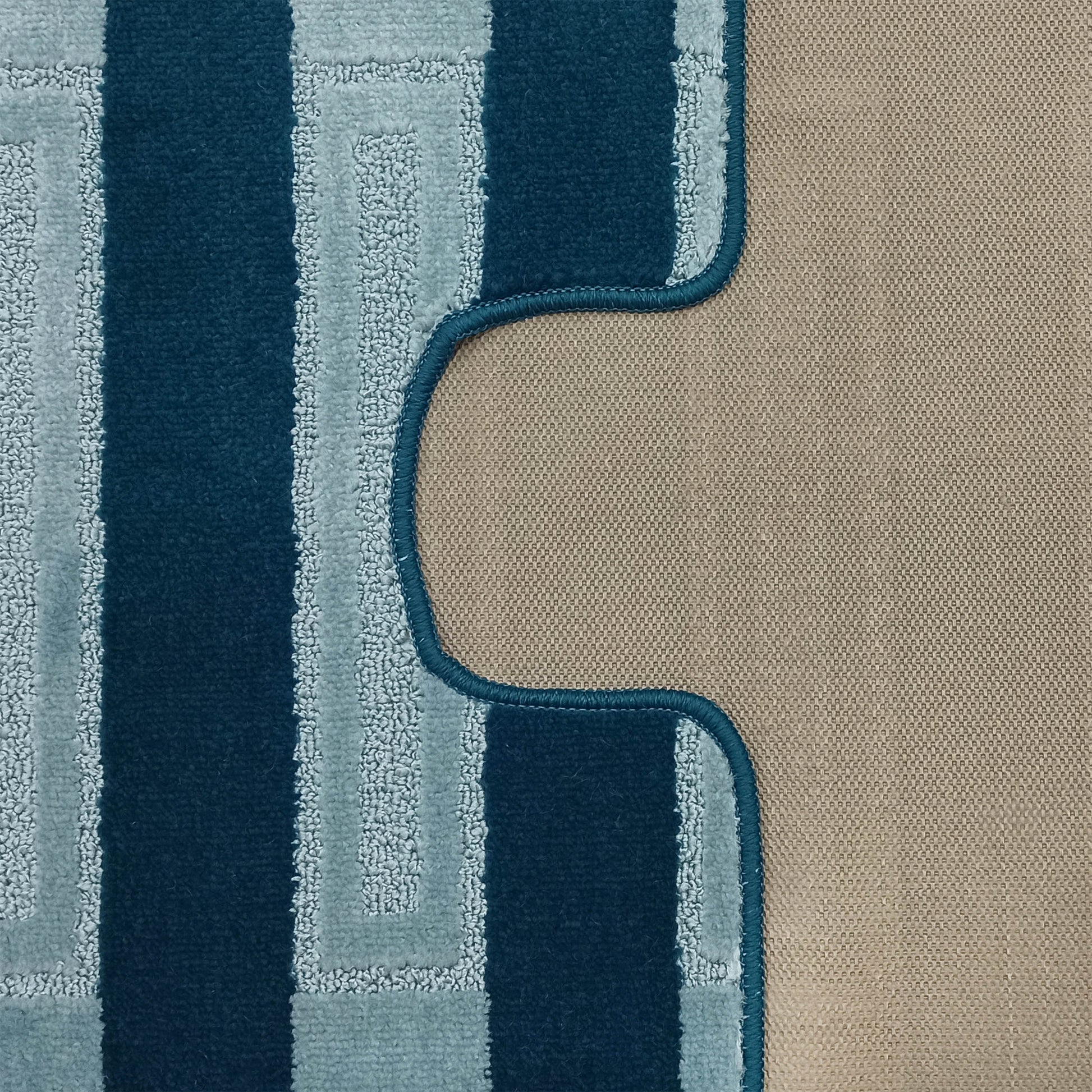 Tapis aux motifs géométriques bleus clairs sur le dessus doux, avec un dos beige texturé et une bordure incurvée cousue