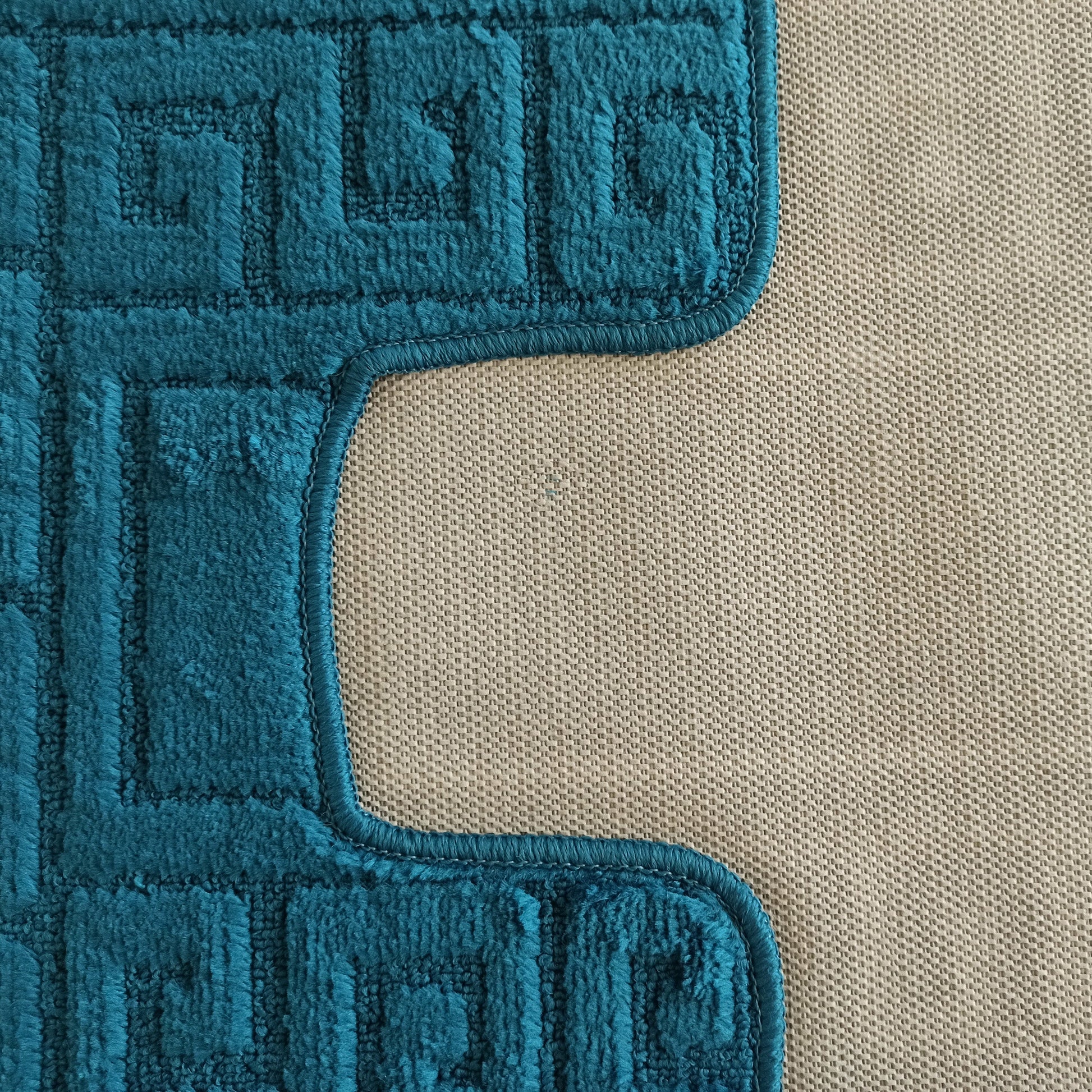 Tapis moelleux bleu sarcelle avec motifs de méandre en relief, visible sur un fond beige texturé