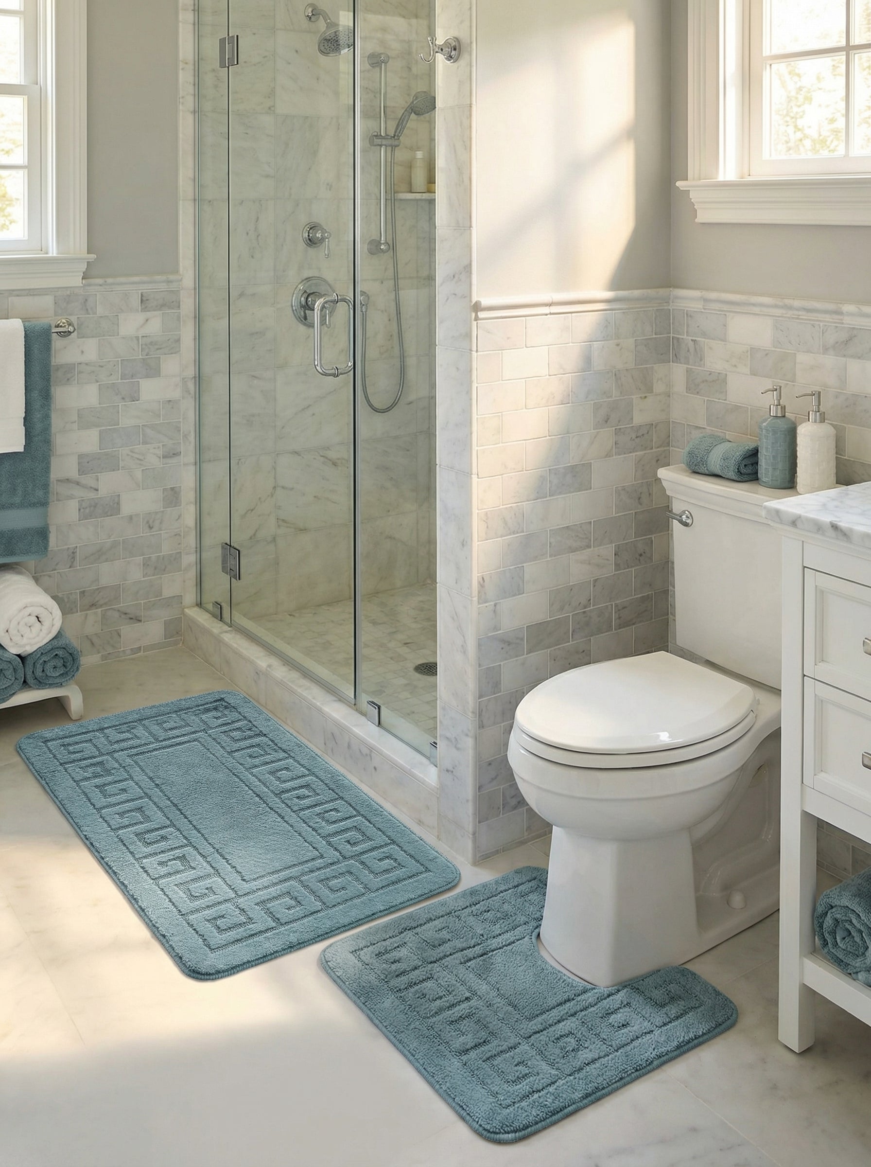 Deux tapis de bain moelleux bleu-vert avec un motif grec, un rectangulaire et un en U, dans une salle de bain claire