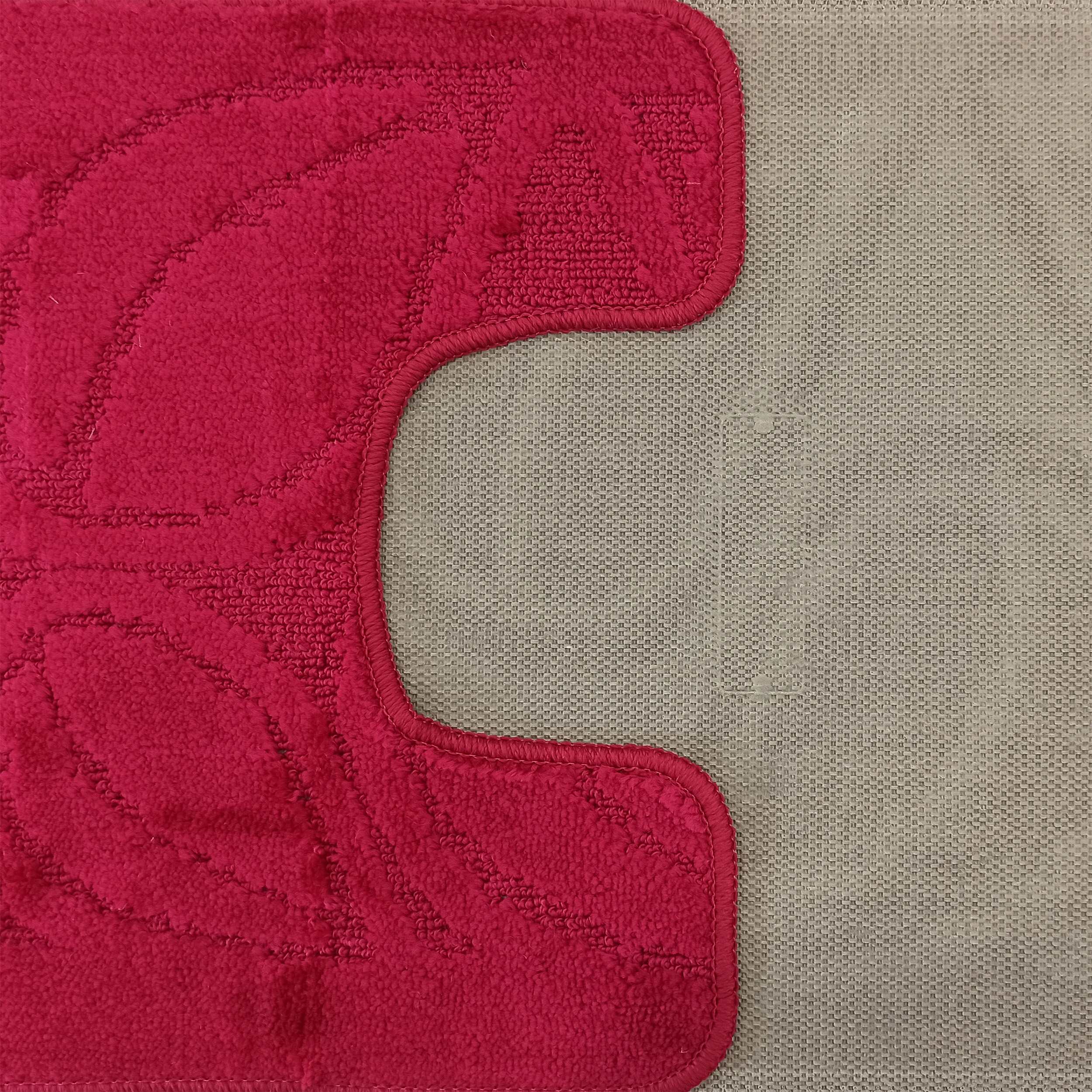 Gros plan sur un tapis rouge vif texturé avec des motifs en relief, posé sur une surface tissée gris clair