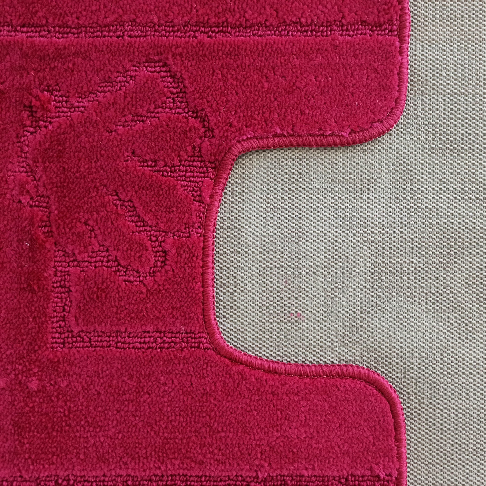 Tapis rose fuchsia épais aux motifs végétaux en relief et bordures courbes, posé sur un sol beige clair texturé