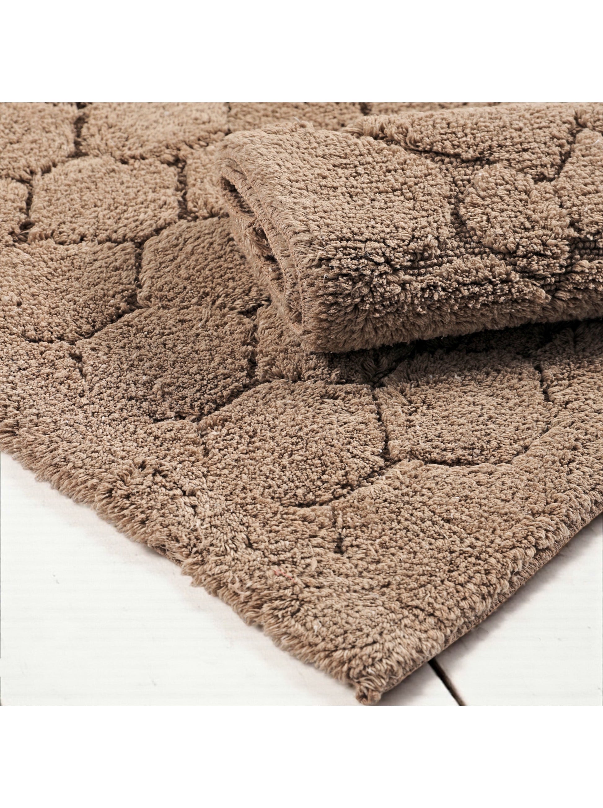 Tapis beige à poils longs avec un motif en relief de formes arrondies, une partie est pliée sur une surface en bois blanc