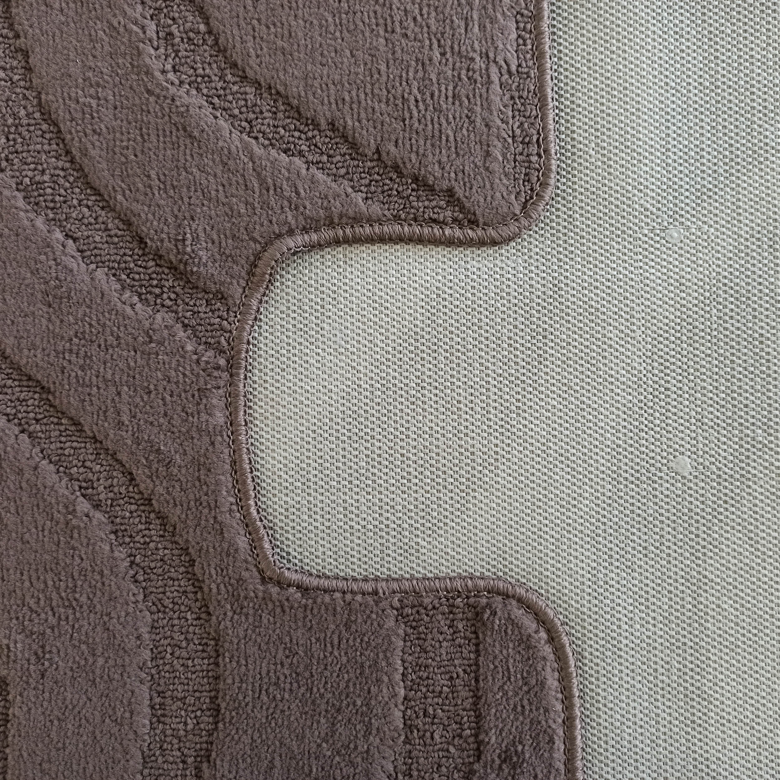 Gros plan d'un tapis en bouclette marron-gris avec motifs ondulés en relief et envers antidérapant tissé clair