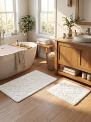 Deux tapis de bain rectangulaires écrus, moelleux, ornés de motifs géométriques en relief, dans une salle de bain lumineuse