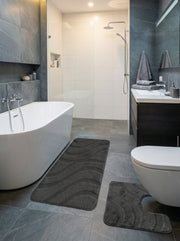 Lot de tapis de bain gris anthracite texturés avec des motifs ondulés, un rectangulaire et un en U, dans une salle de bain moderne
