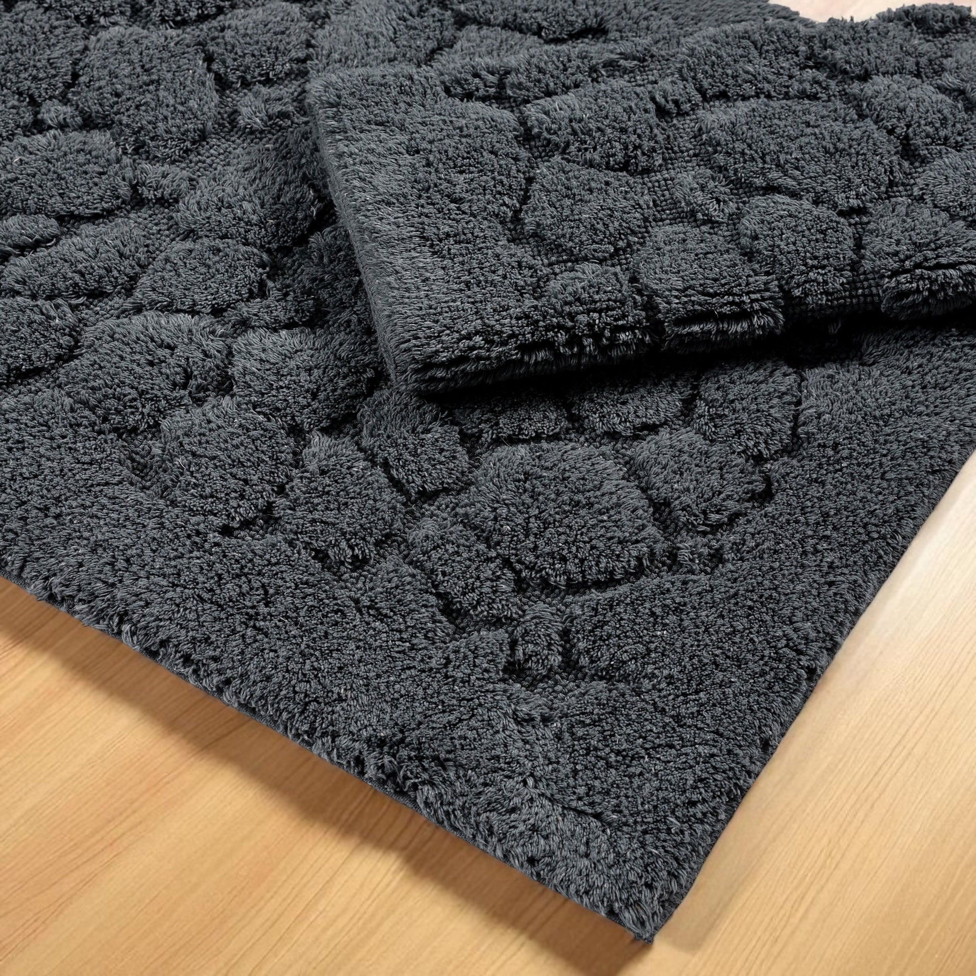 Deux tapis gris foncé à motifs bouclés en relief de galets, posés sur un sol en bois clair