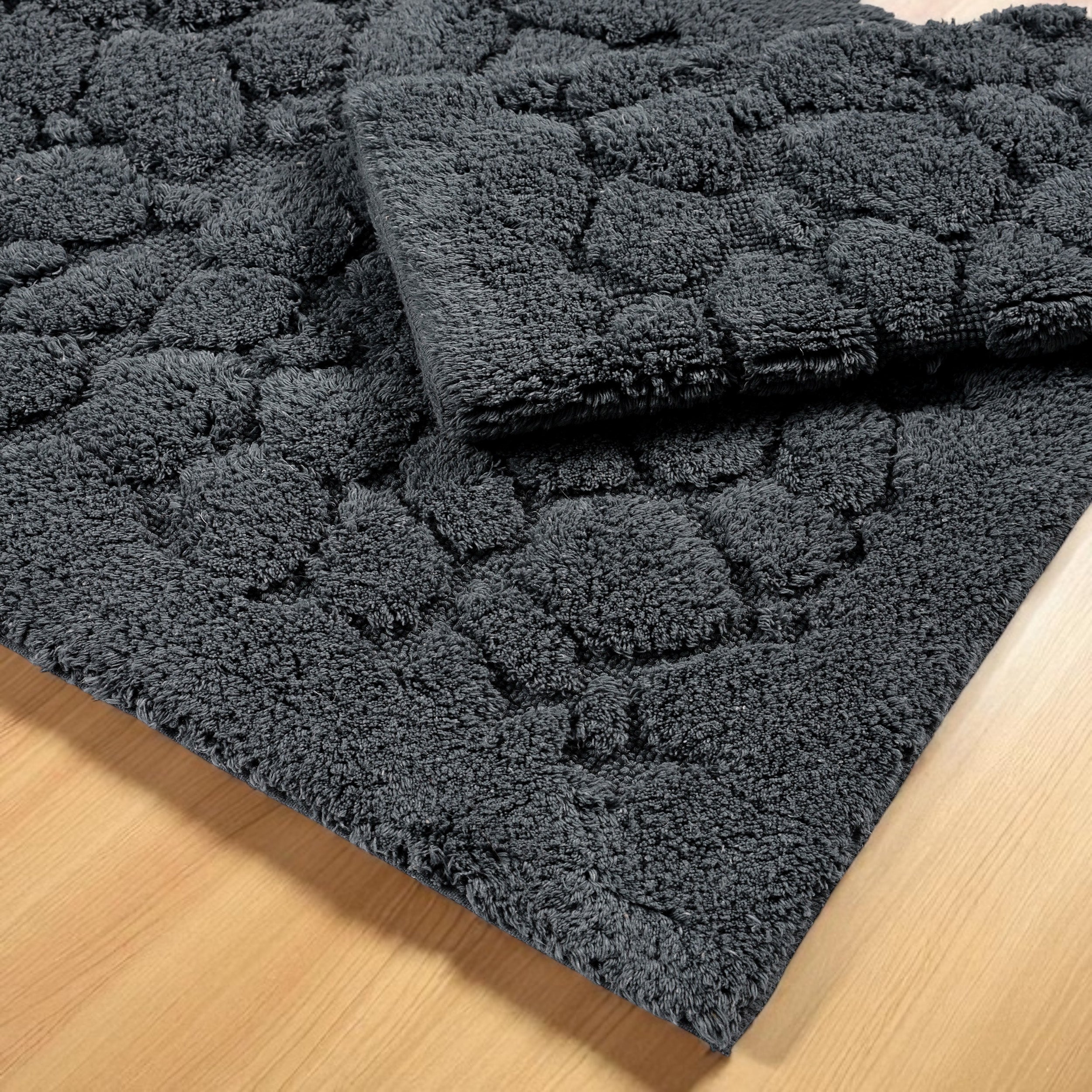 Deux tapis gris foncé à motifs bouclés en relief de galets, posés sur un sol en bois clair