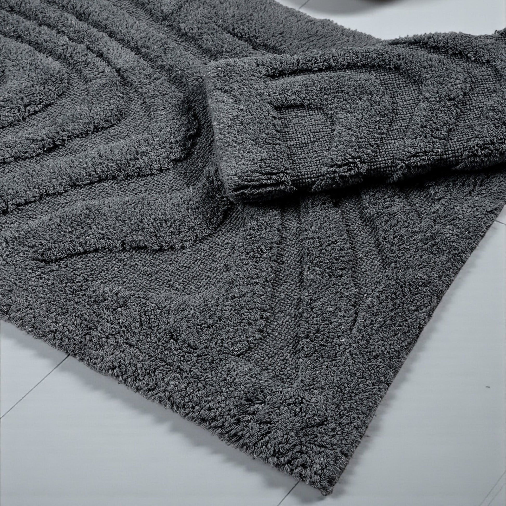 Tapis gris anthracite à la texture dense et bouclée, avec des motifs géométriques en relief, posé sur un sol clair