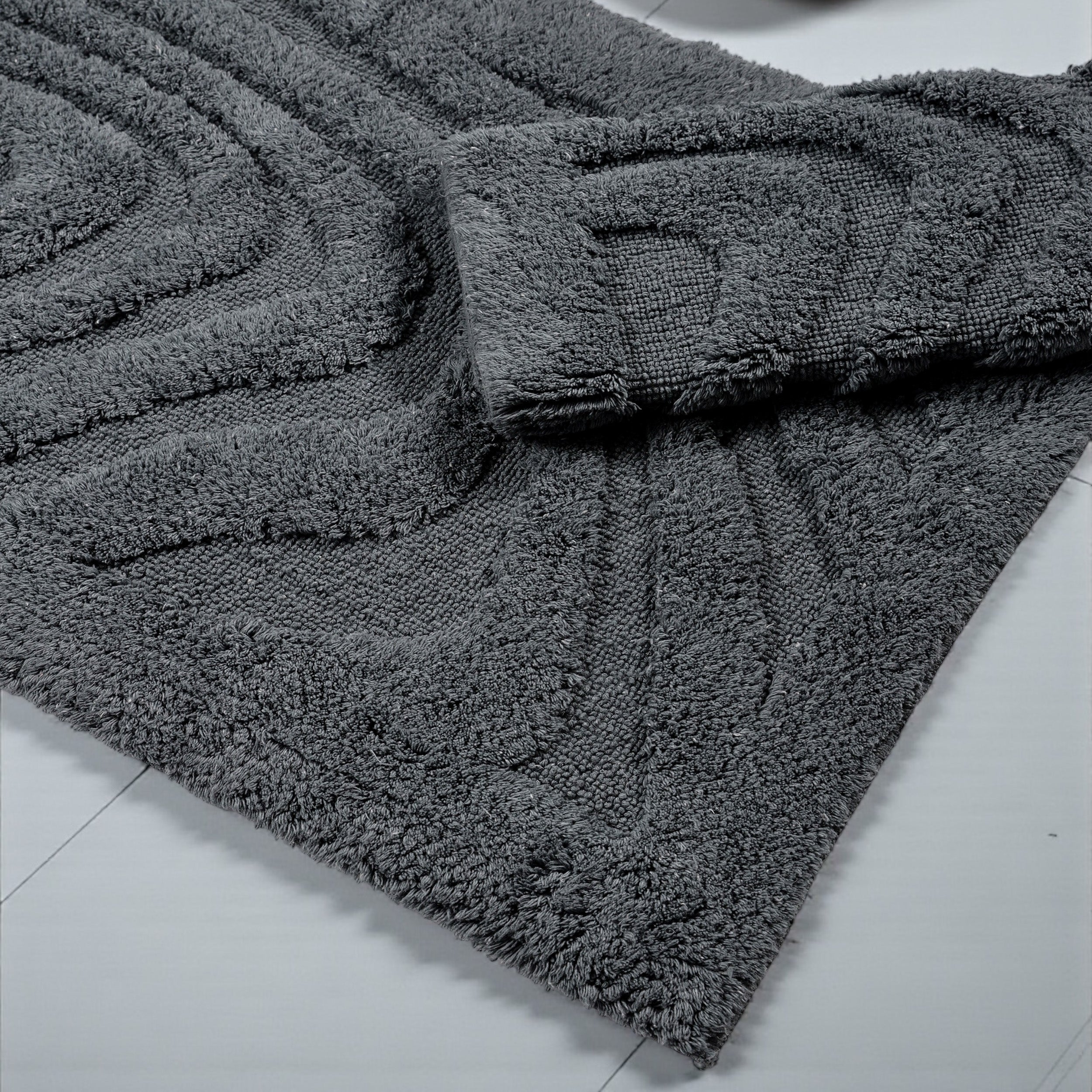 Tapis gris anthracite à la texture dense et bouclée, avec des motifs géométriques en relief, posé sur un sol clair