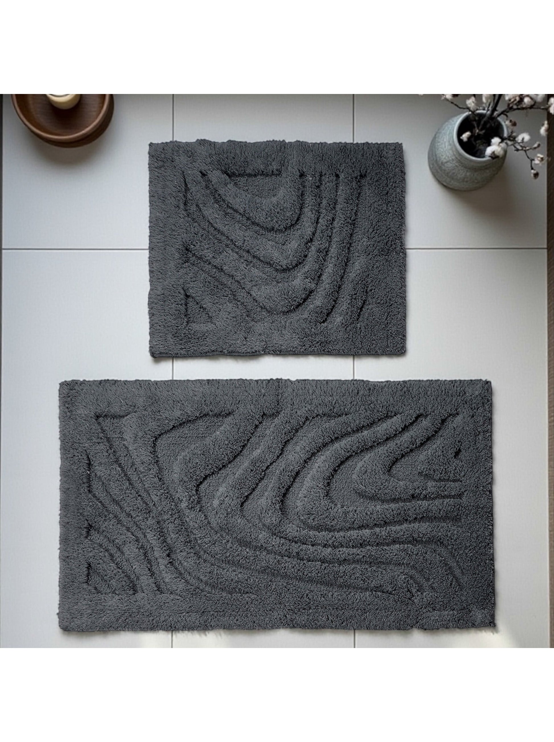 Deux tapis gris foncé en matière bouclée avec des motifs ondulés en relief sur un sol carrelé clair