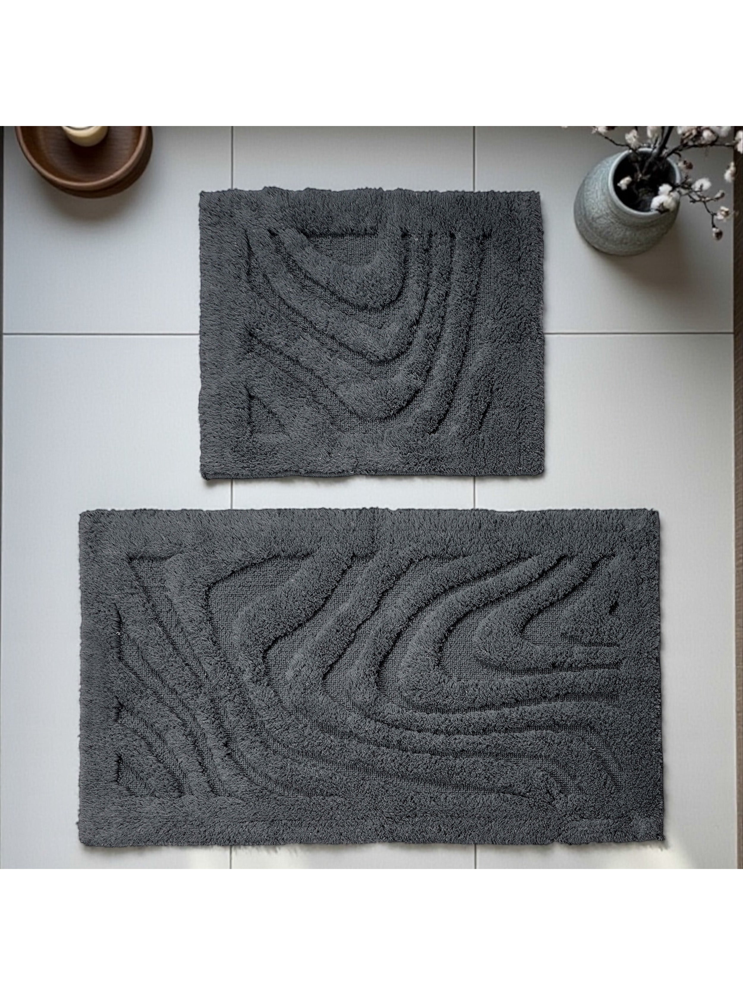 Deux tapis gris foncé en matière bouclée avec des motifs ondulés en relief sur un sol carrelé clair