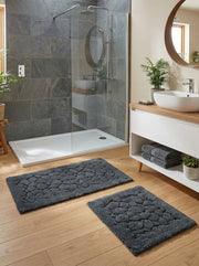 Deux tapis de bain rectangulaires gris foncé avec un relief en forme de galets, posés sur un parquet dans une salle de bain moderne