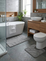 Deux tapis de bain gris avec motifs vagues, un rectangulaire et un en U, posés sur un sol carrelé dans une salle de bain moderne
