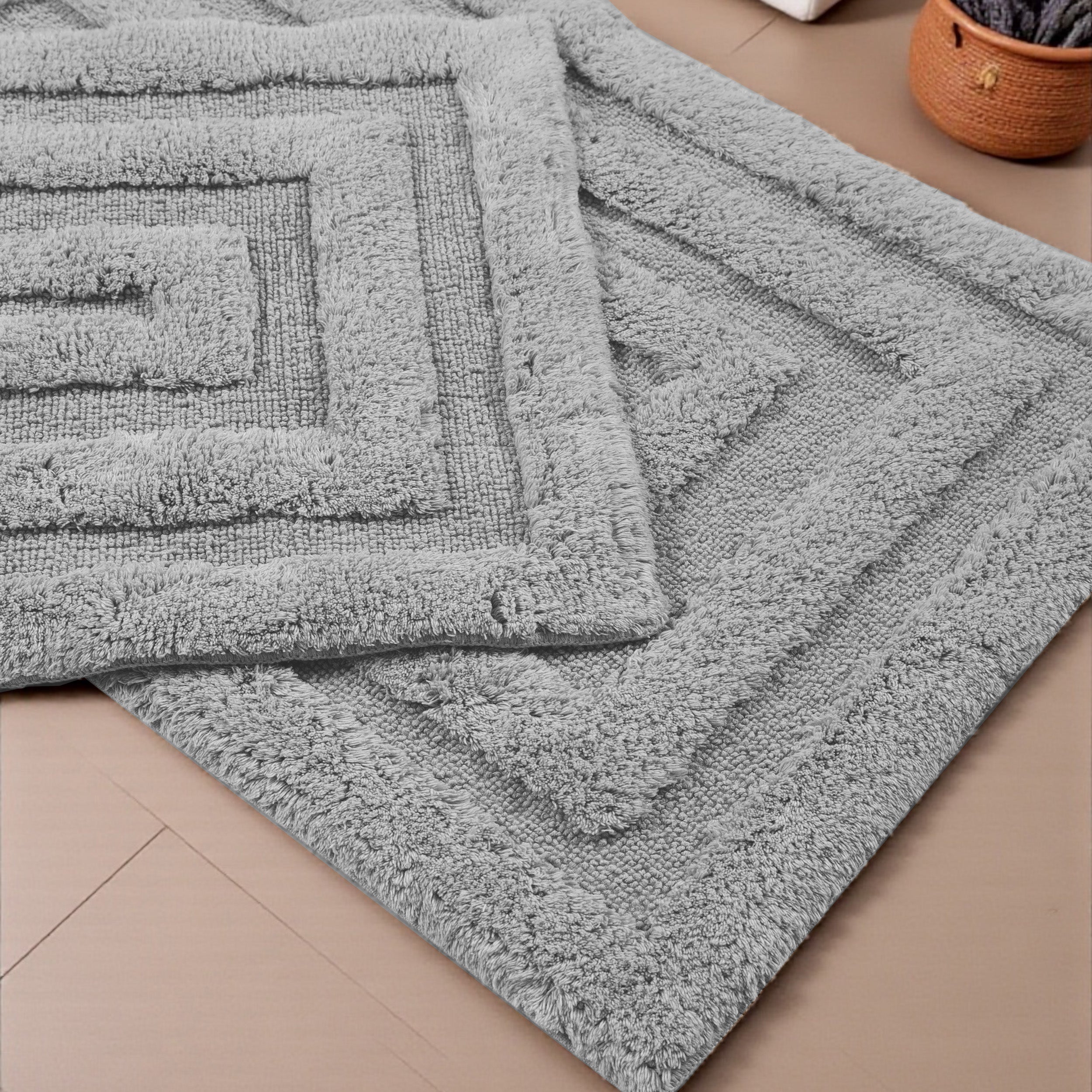 Deux tapis gris en tissu bouclé, l'un sur l'autre, avec des motifs de carrés concentriques en relief