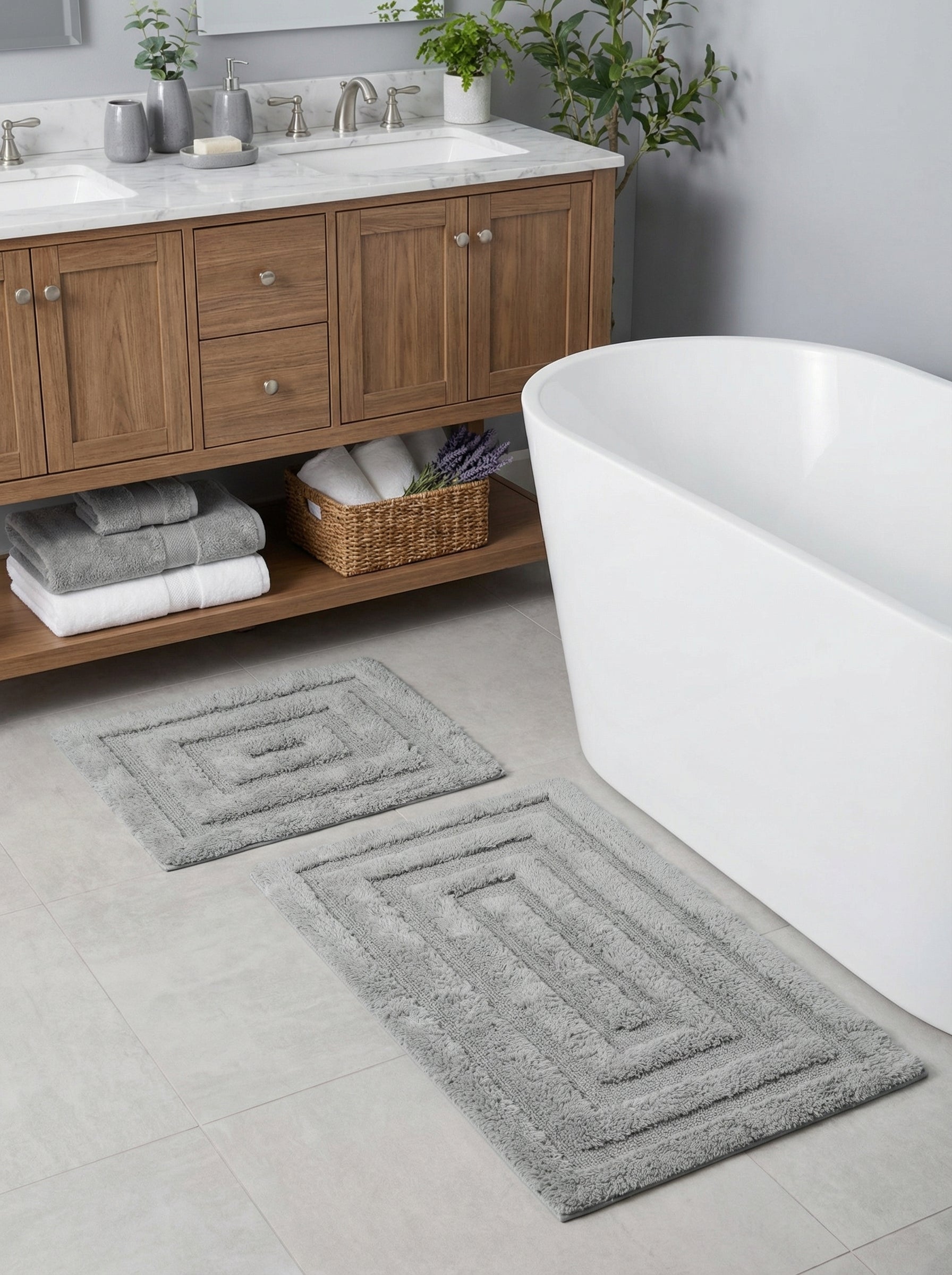 Deux tapis de bain gris rectangulaires en éponge avec des motifs concentriques en relief, sur le carrelage clair d'une salle de bain moderne