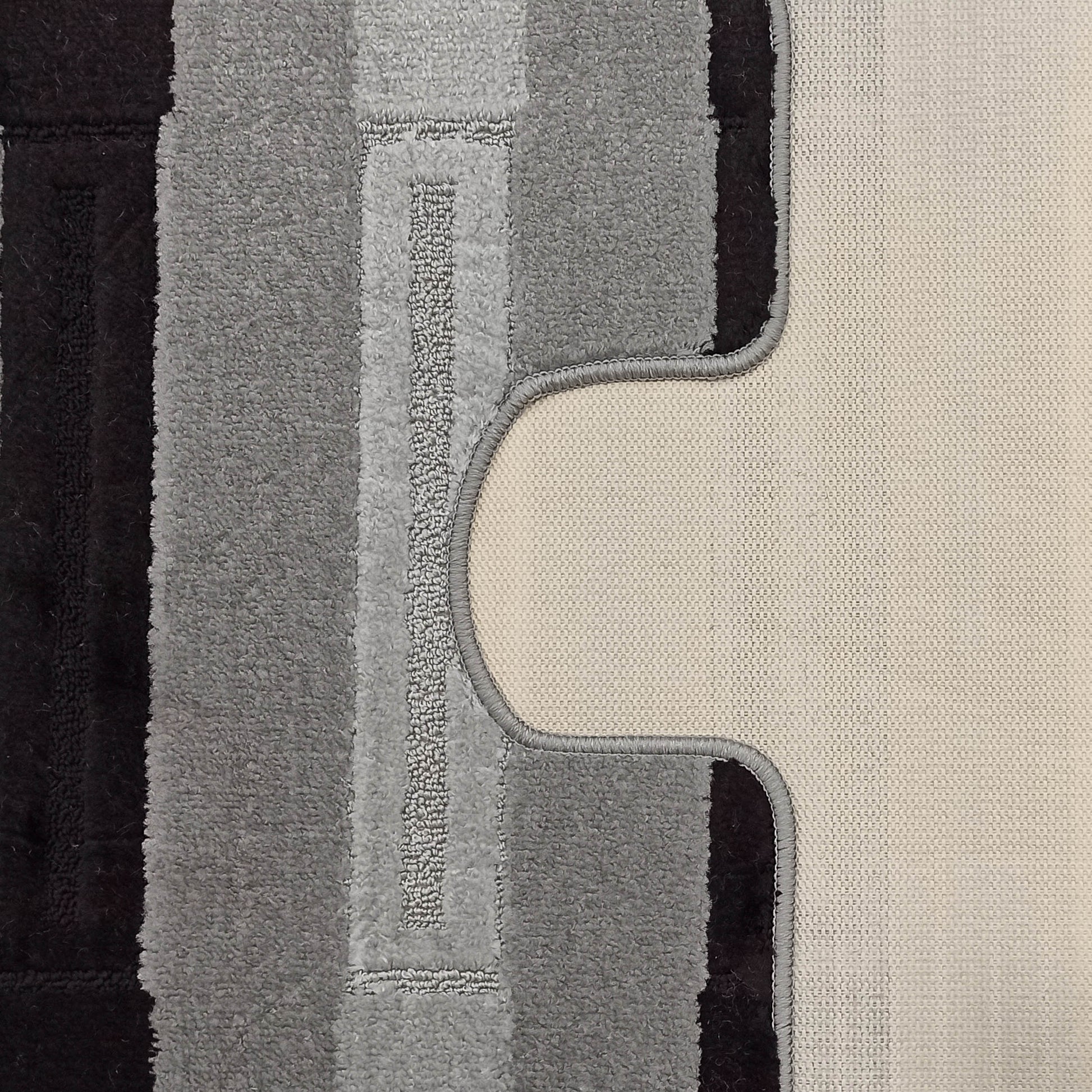 Tapis texturé à rayures verticales noires et grises, dont le dos clair en tissu tissé est visible sur la droite, présentant une découpe incurvée et son galon gris