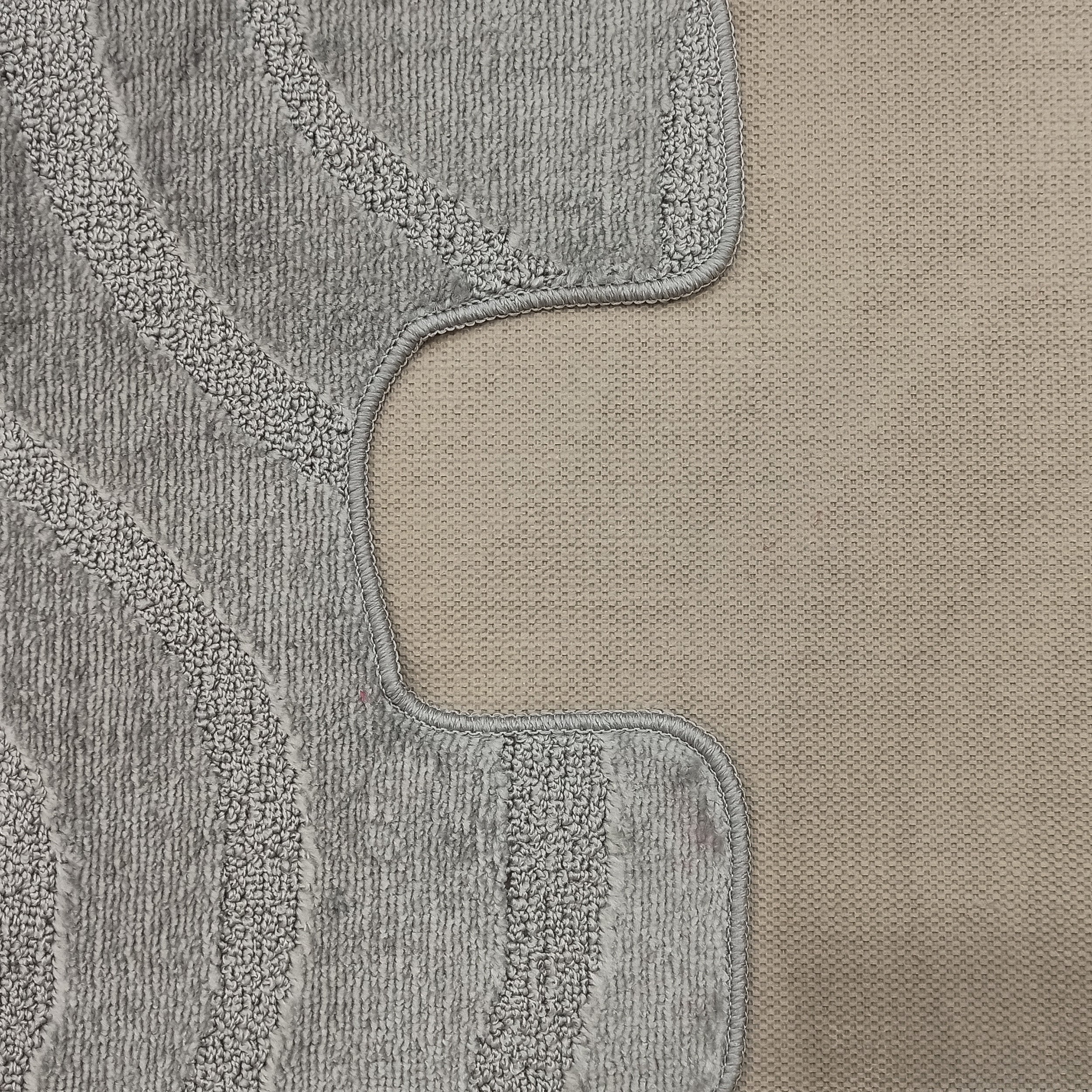 Tapis gris en bouclettes avec des motifs ondulés en relief, sa bordure courbe surpiquée borde un sol beige tissé