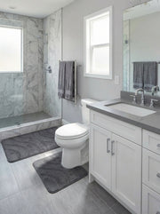 Deux tapis de bain gris anthracite moelleux avec des motifs de vagues sombres ornent le sol d'une salle de bain lumineuse