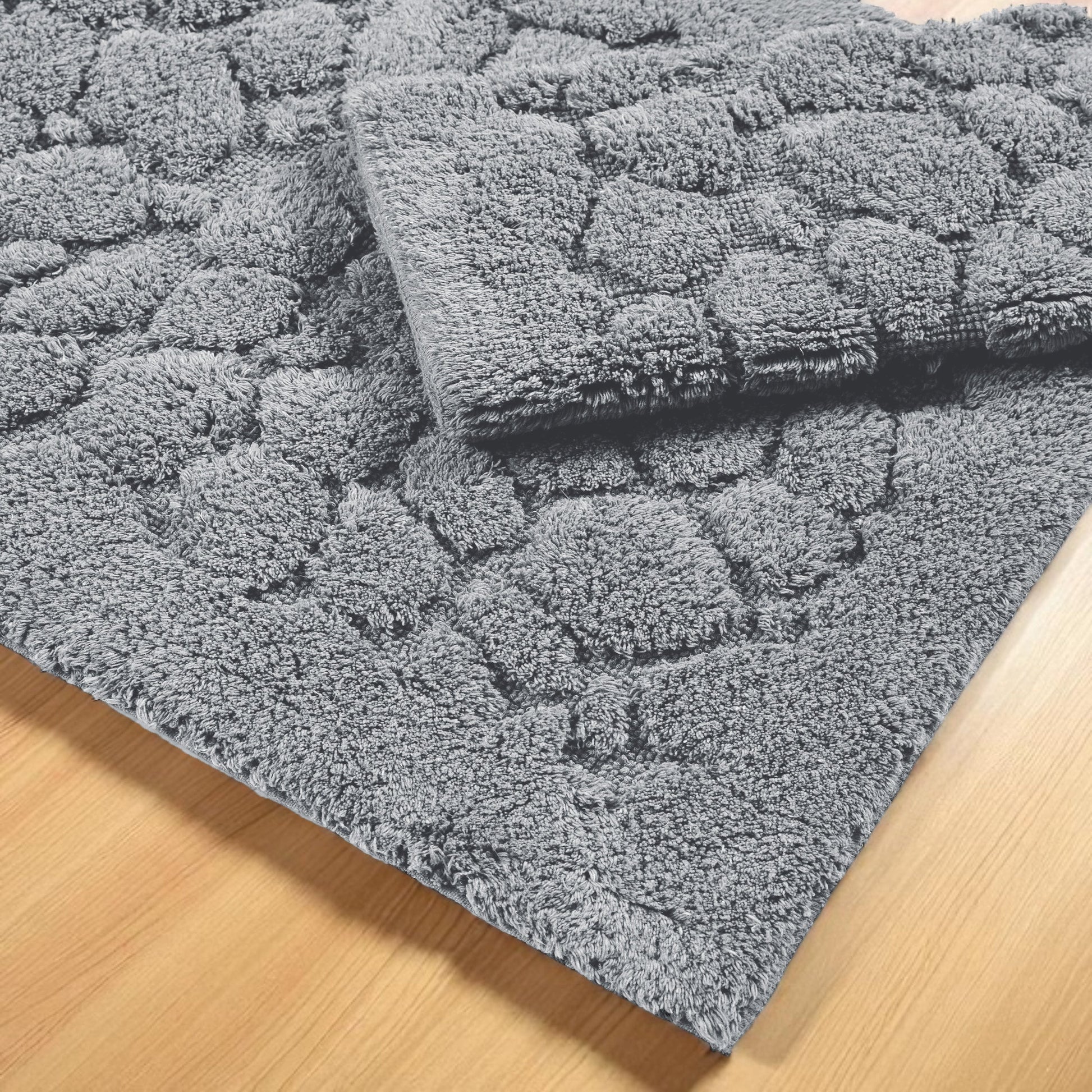 Deux tapis gris à texture douce et bouclée avec des motifs en relief, posés sur un parquet en bois clair