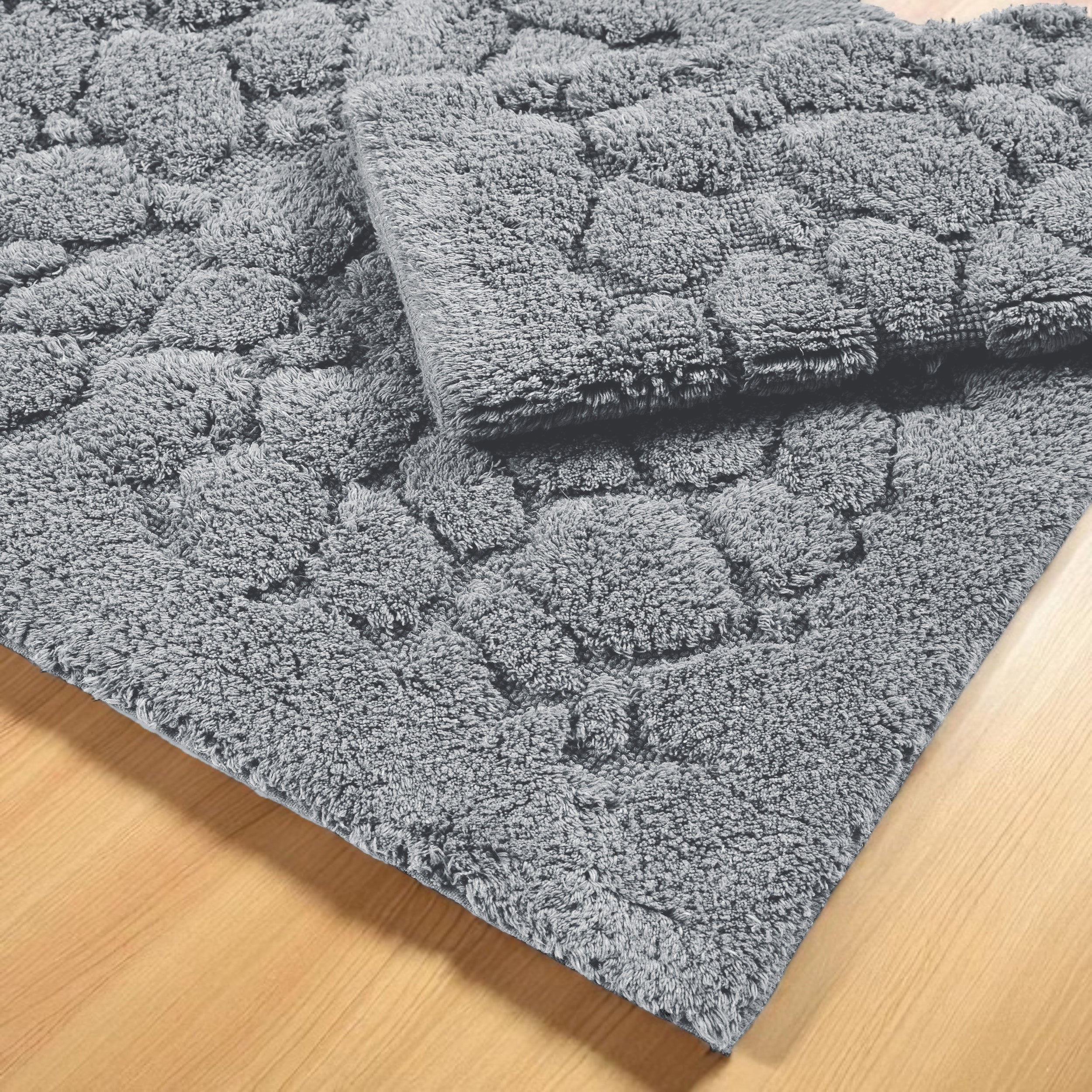 Deux tapis gris à texture douce et bouclée avec des motifs en relief, posés sur un parquet en bois clair