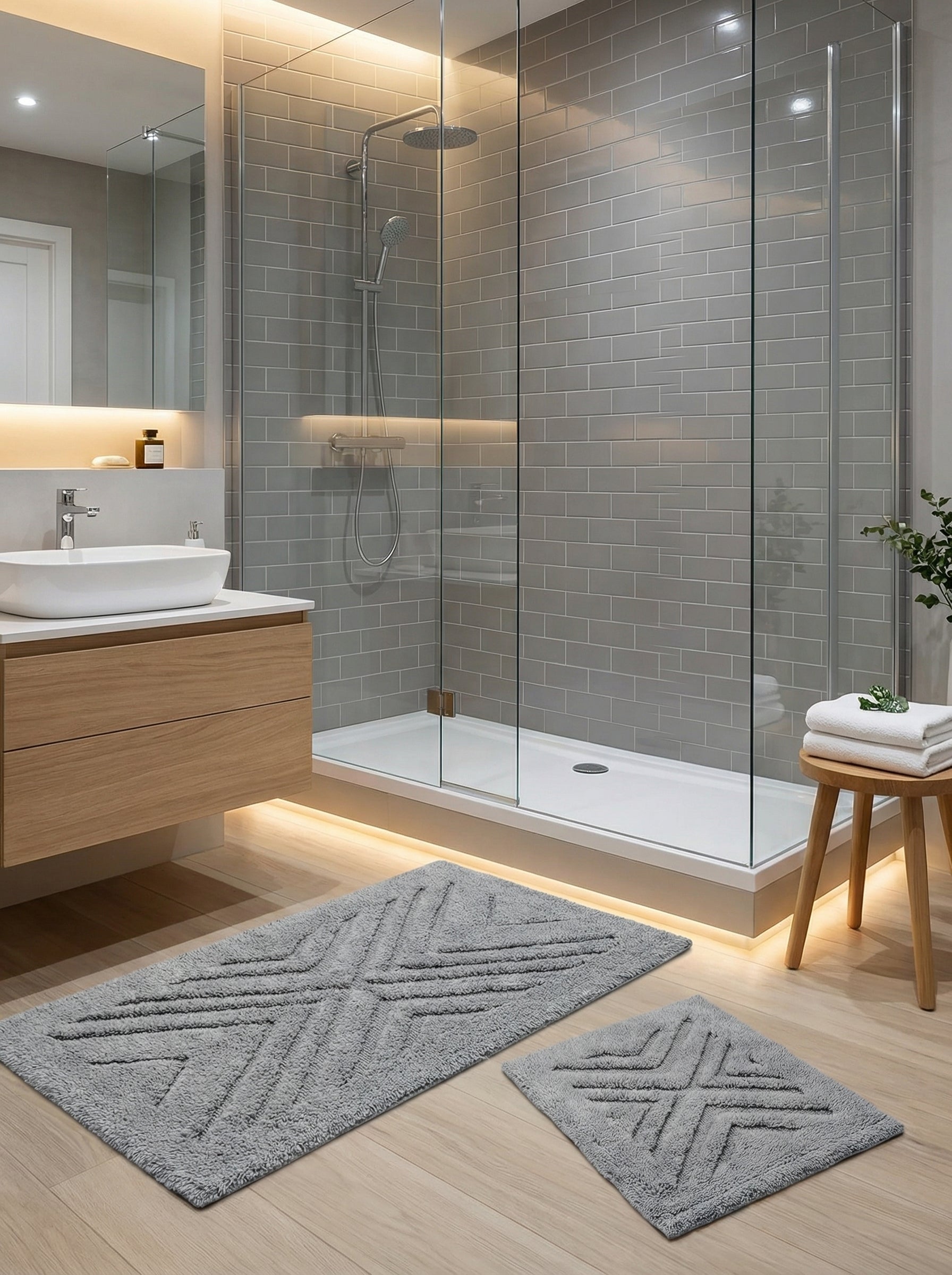 Deux tapis de bain gris à motifs géométriques en relief sont posés sur un parquet clair dans une salle de bain moderne