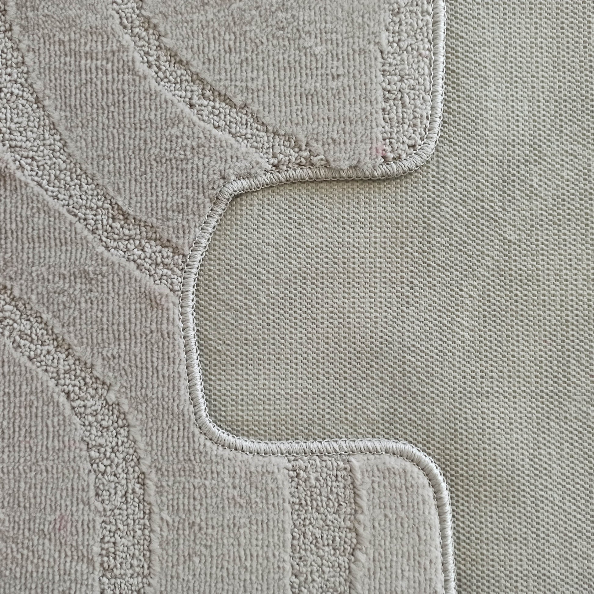 Gros plan d'un tapis beige texturé avec des motifs curvilignes en bouclettes et une partie à poils courts, bordé d'un dos tissé