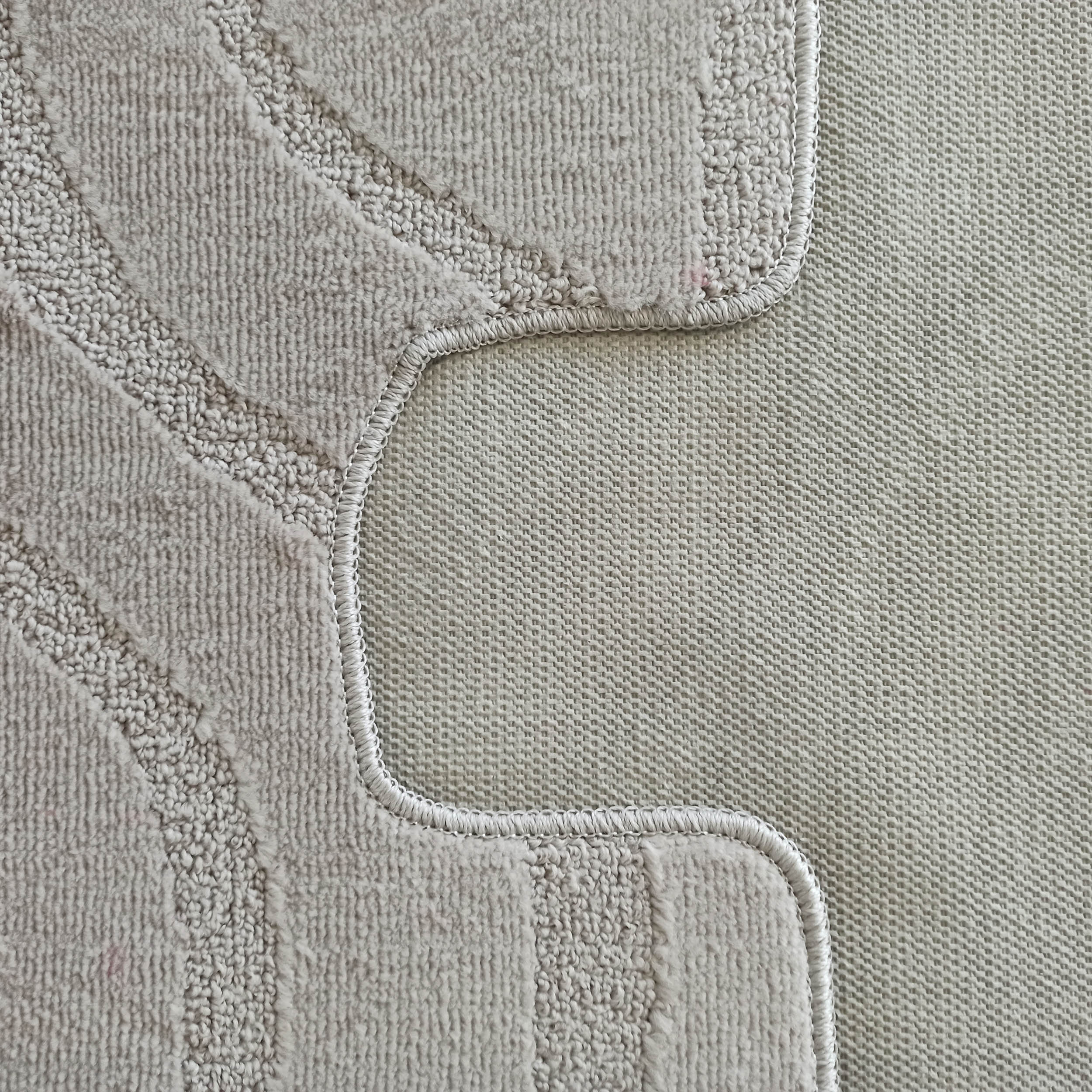 Gros plan d'un tapis beige texturé avec des motifs curvilignes en bouclettes et une partie à poils courts, bordé d'un dos tissé