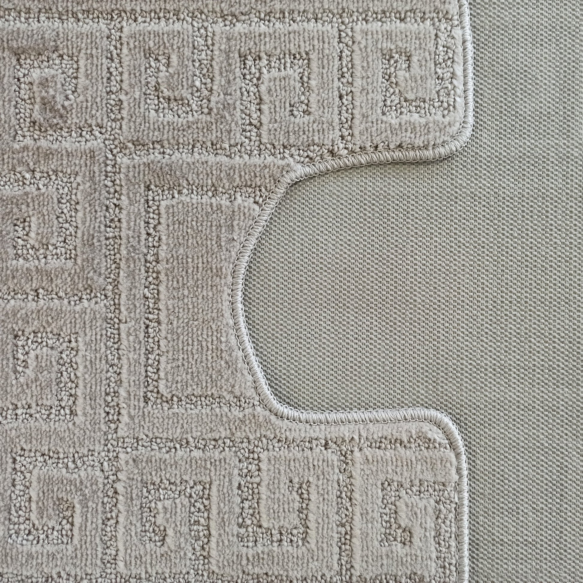 Tapis beige clair à motifs géométriques en méandre avec une texture bouclée, bordé d'une couture et découpé en courbe, révélant un tissage fin