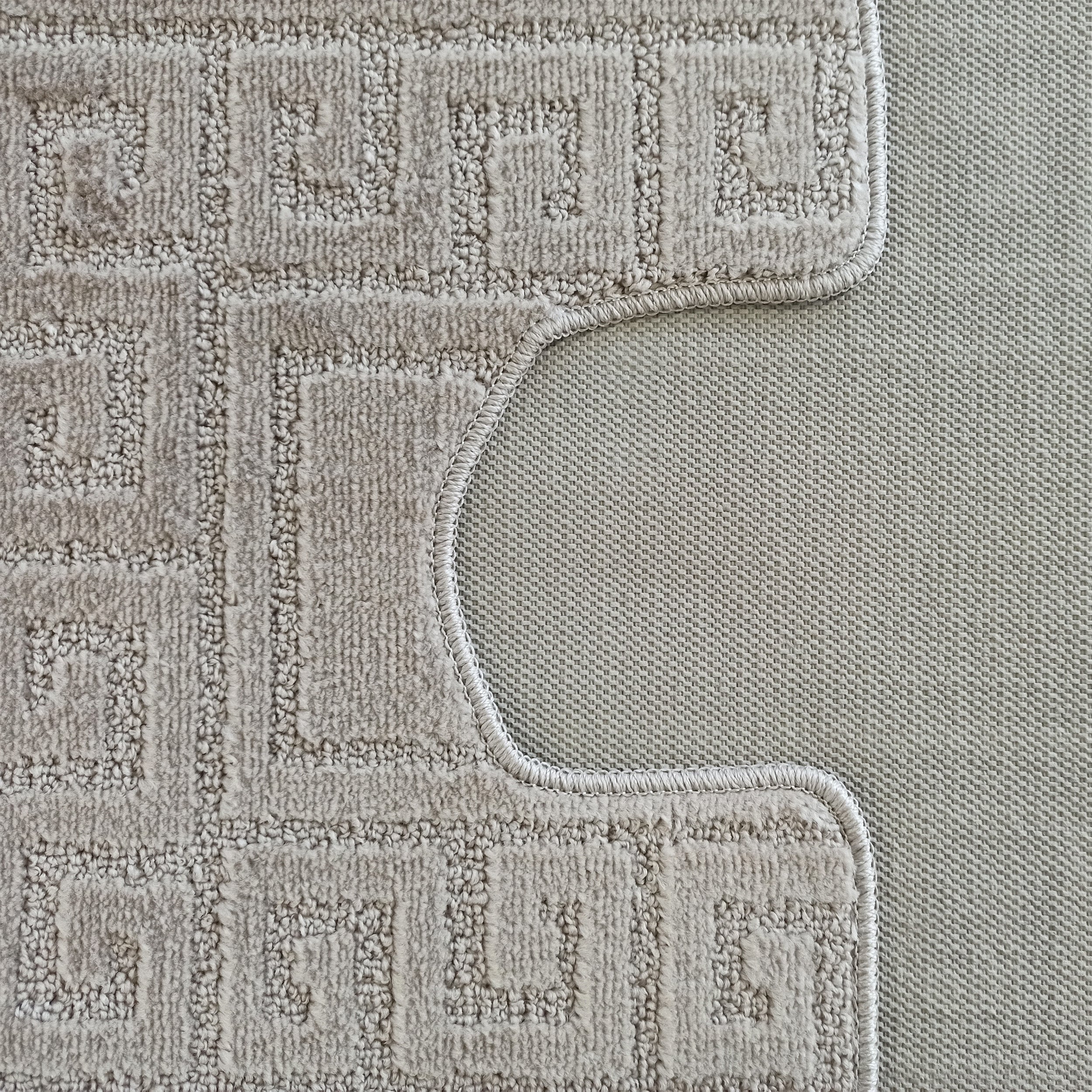 Tapis beige clair à motifs géométriques en méandre avec une texture bouclée, bordé d'une couture et découpé en courbe, révélant un tissage fin