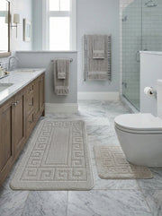 Deux tapis de bain beige clair en coton bouclé, avec motif grecque en relief sur les bordures, posés dans une salle de bain élégante