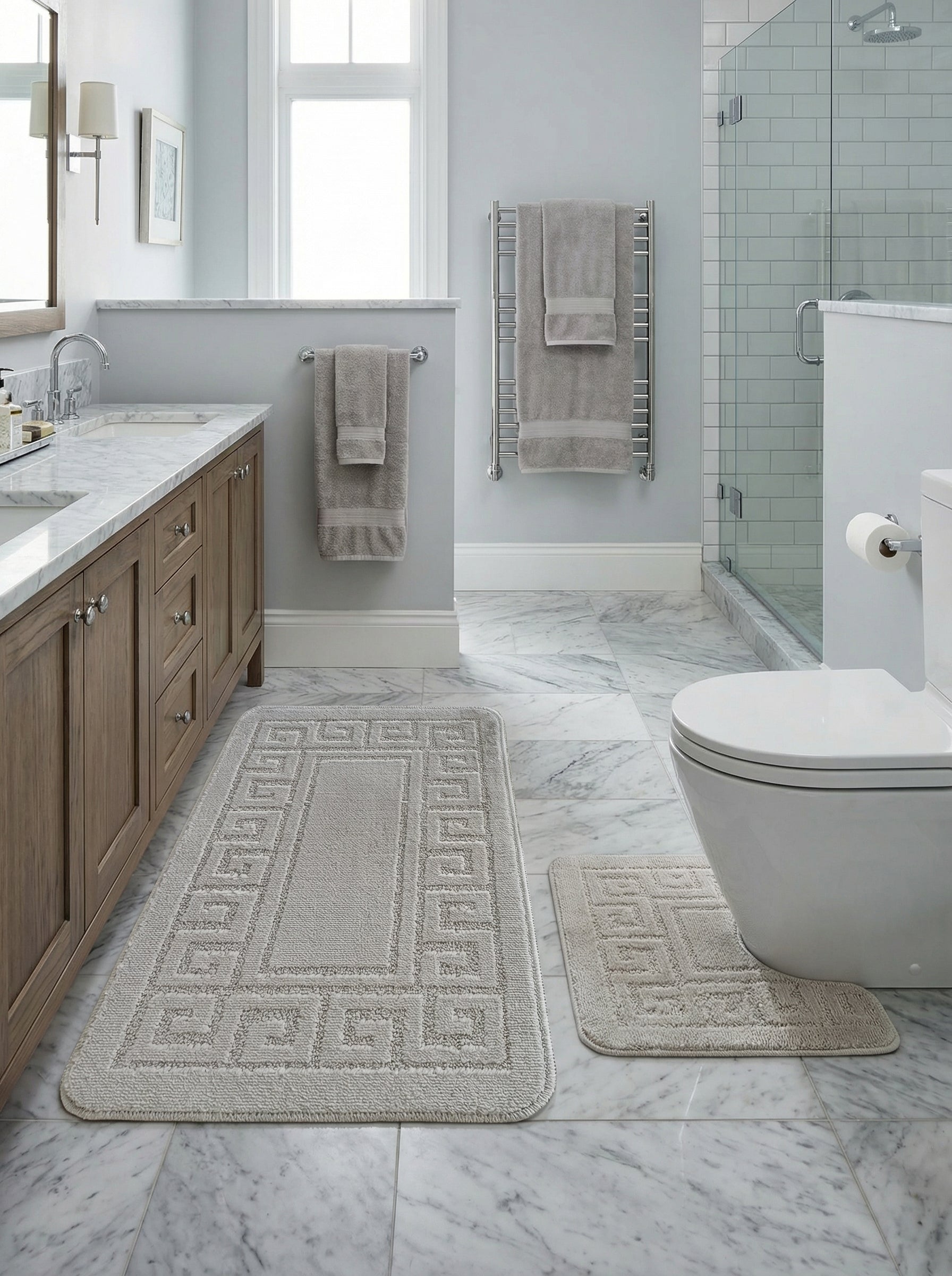 Deux tapis de bain beige clair en coton bouclé, avec motif grecque en relief sur les bordures, posés dans une salle de bain élégante