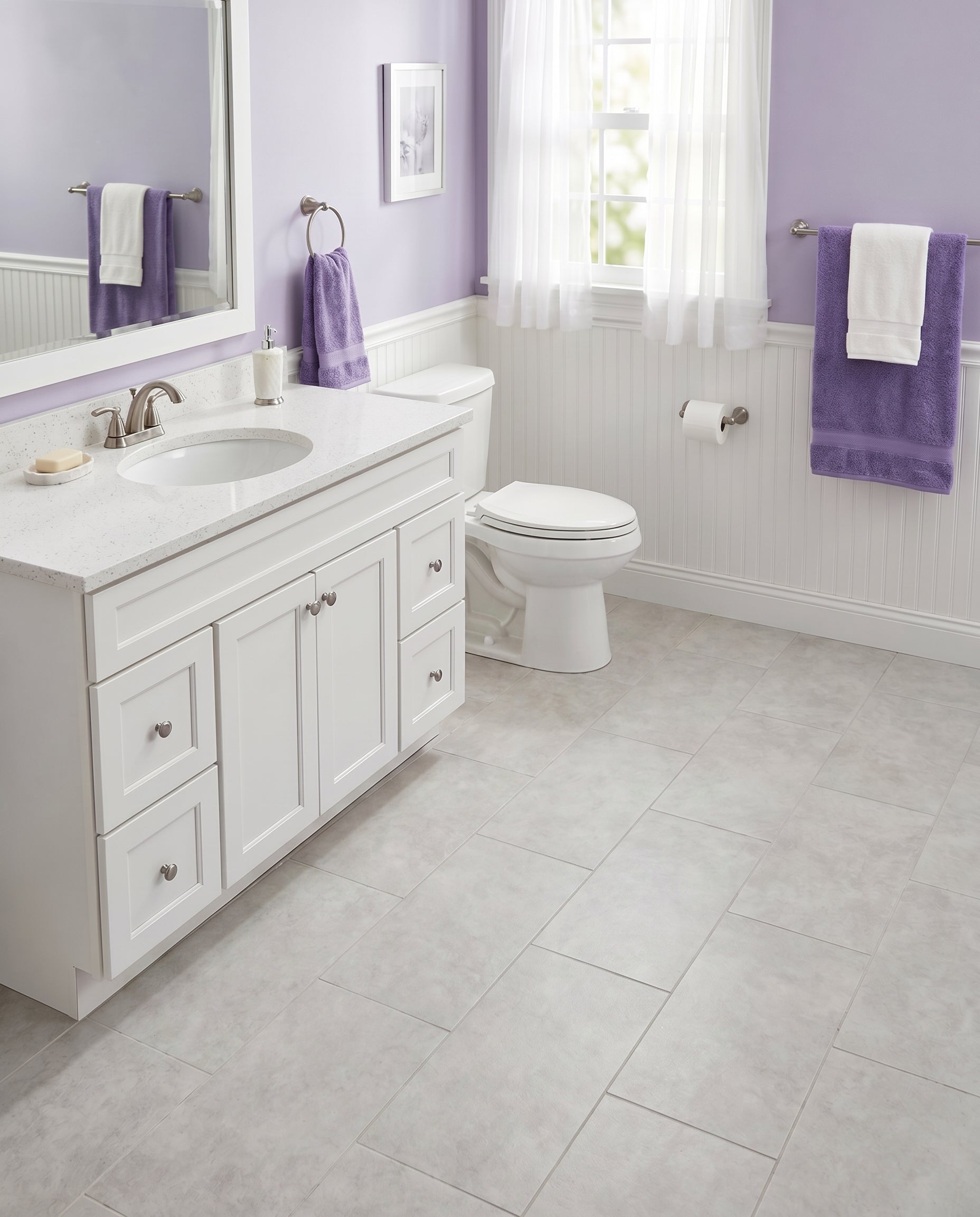 Salle de bain aux murs mauves et lambris blancs, sol carrelé gris clair. Meuble-lavabo, toilettes, miroir et serviettes mauves