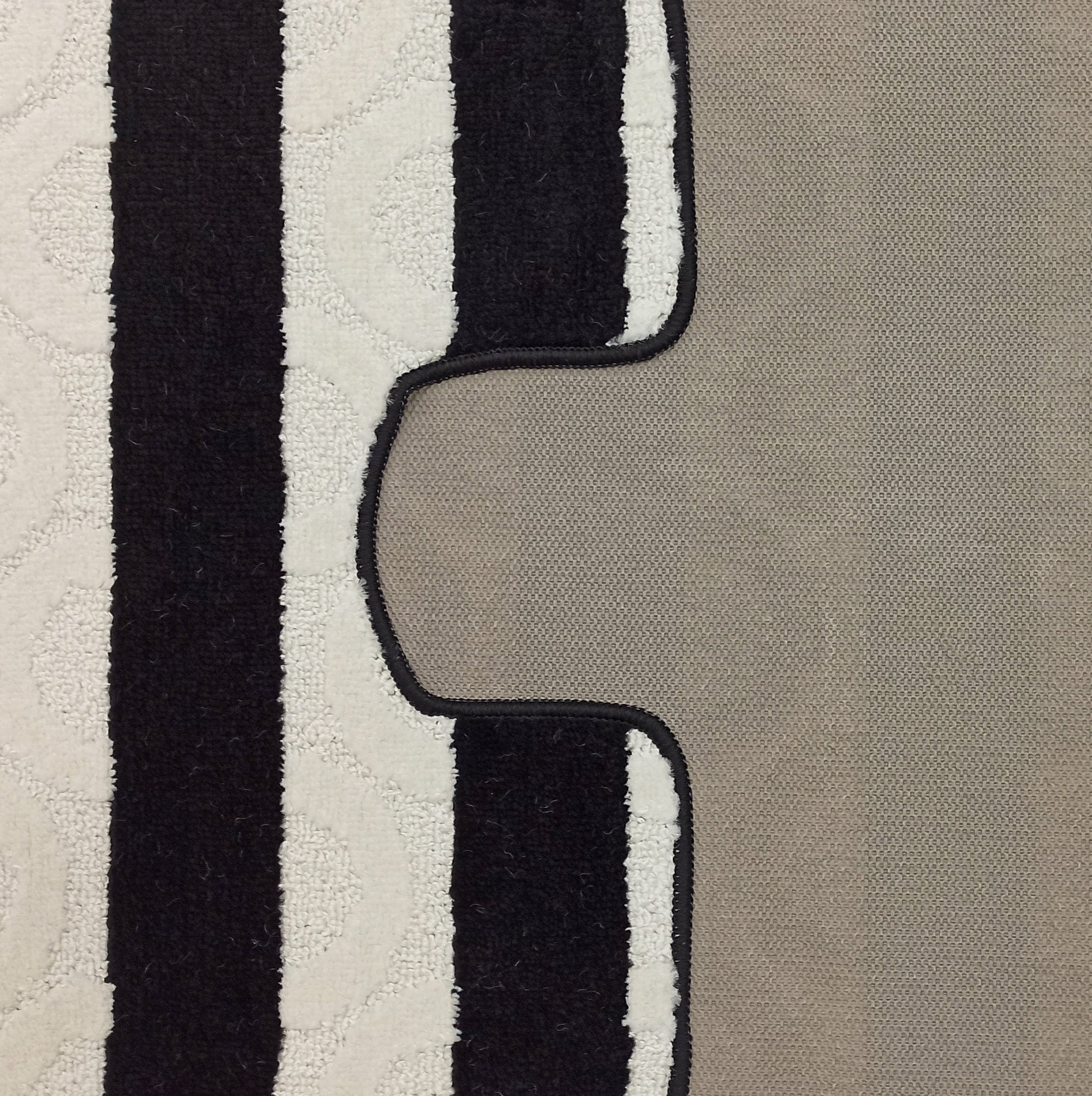 Tapis texturé bouclé à rayures verticales alternées noires et blanches avec des motifs discrets, bordé de noir sur un fond beige