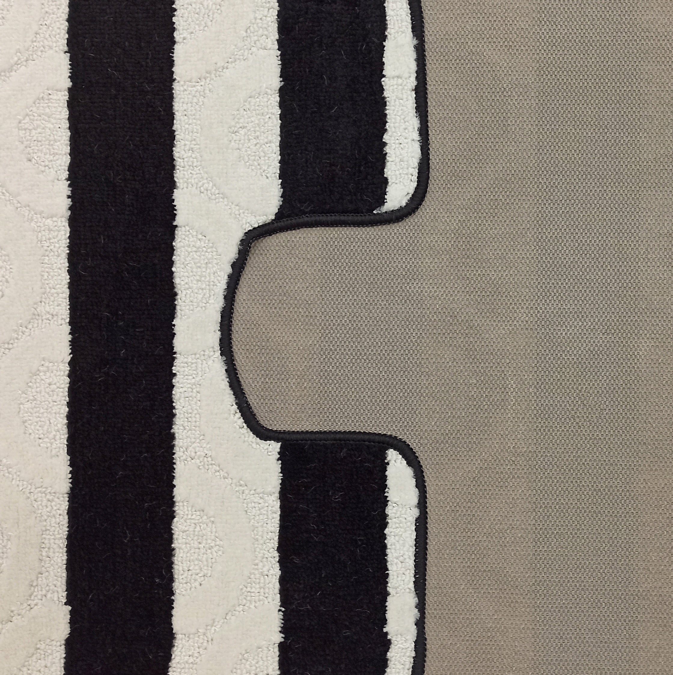 Tapis texturé bouclé à rayures verticales alternées noires et blanches avec des motifs discrets, bordé de noir sur un fond beige